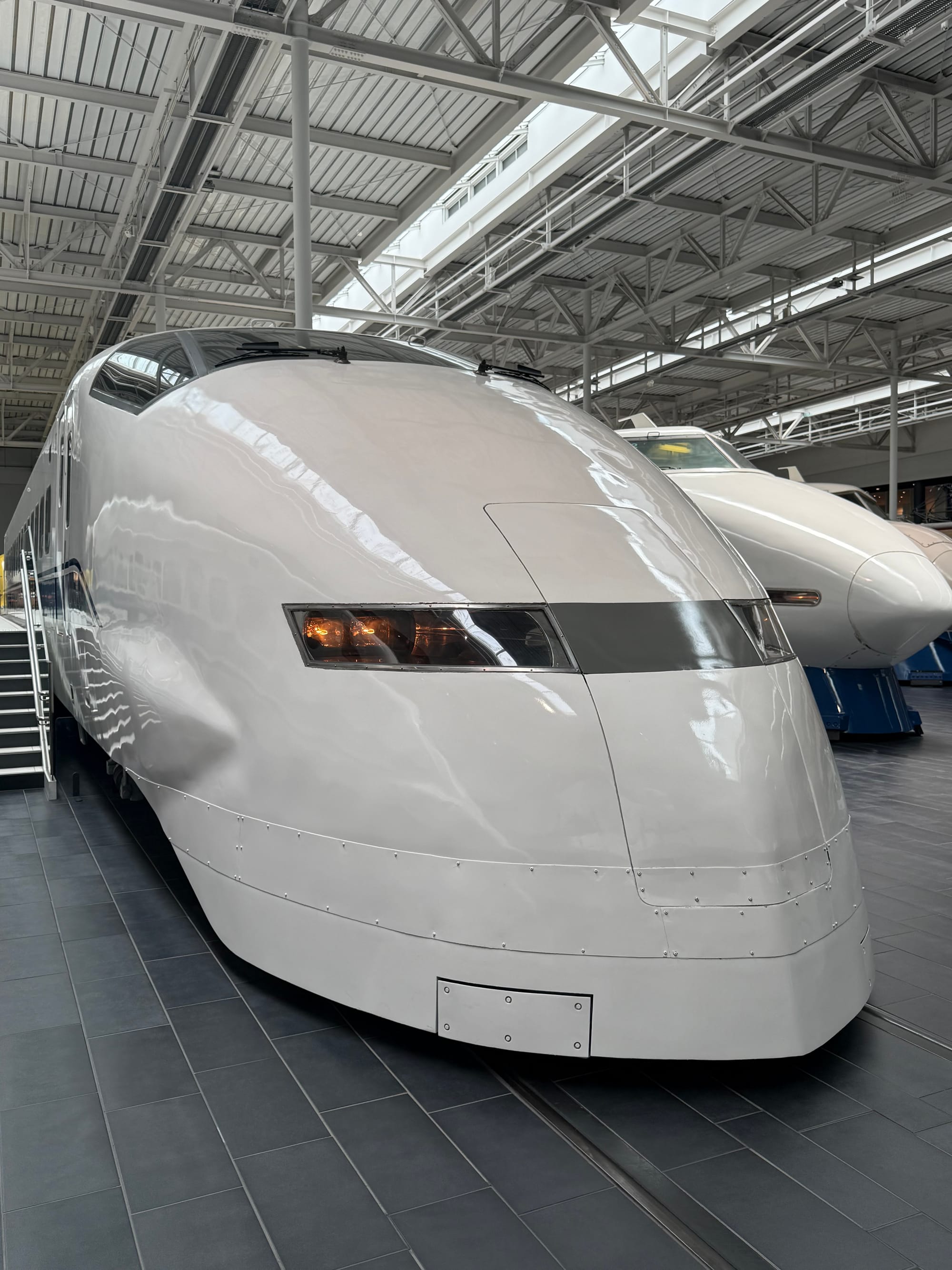 300 Series Shinkansen displayed at the SCMAGLEV and Railway Park in Nagoya, featuring its aerodynamic wedge-shaped nose and smooth white bodywork inside the museum hall.