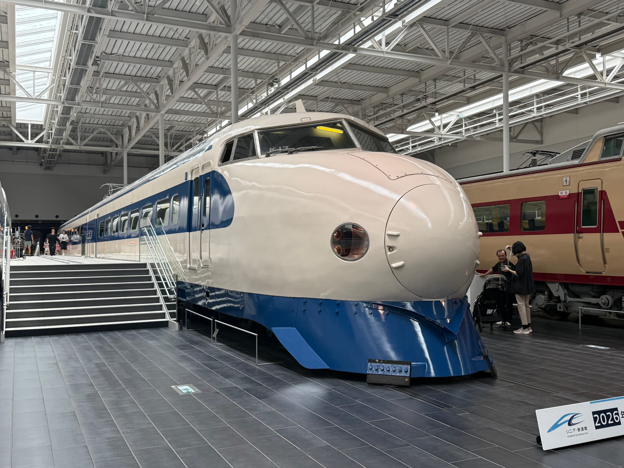Alt text (under 191 characters):  0 Series Shinkansen displayed at the SCMAGLEV and Railway Park in Nagoya, featuring its iconic rounded nose and blue-and-white livery inside the museum's railway hall.