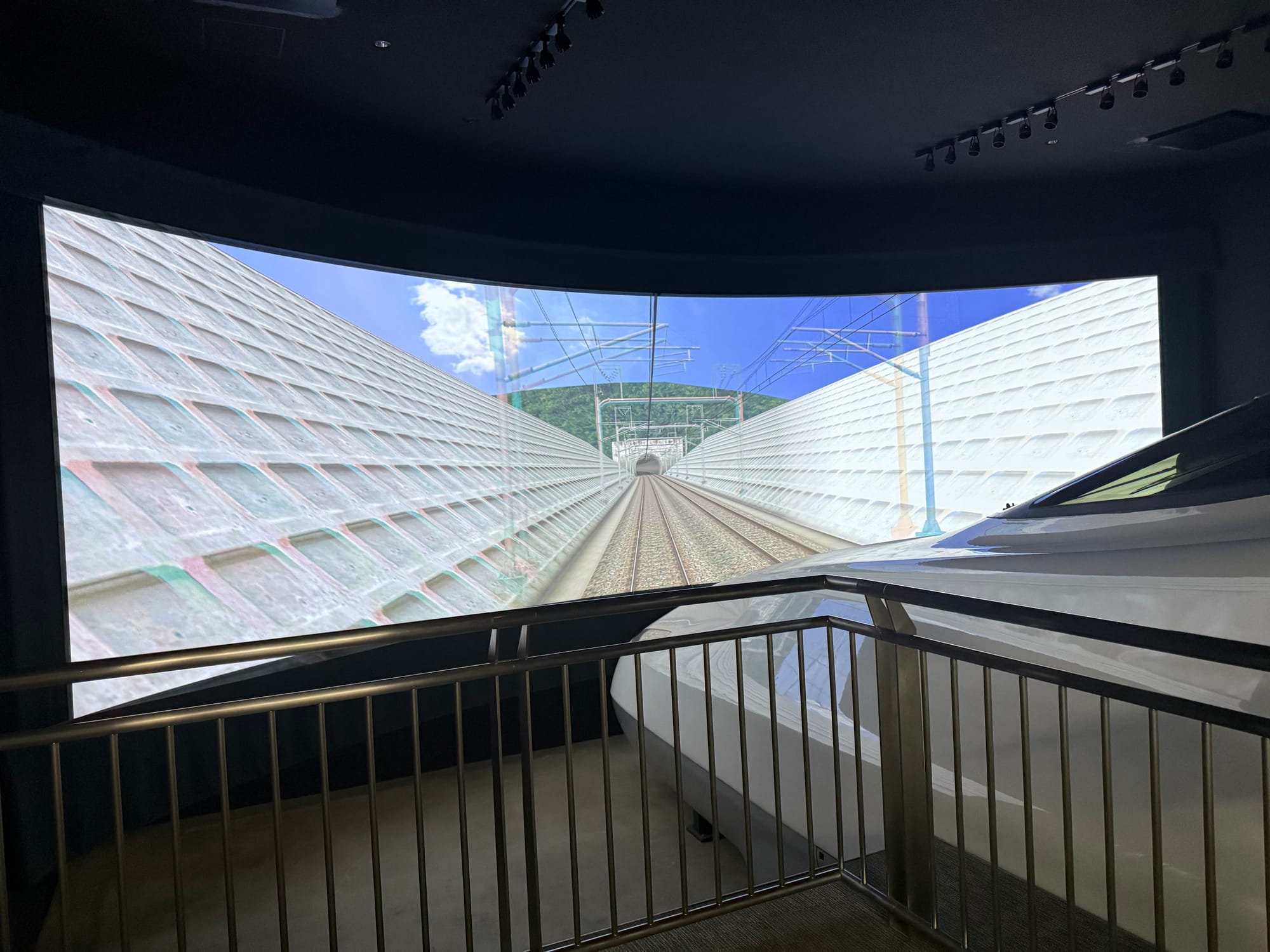 Large Shinkansen driving simulator at the SCMAGLEV and Railway Park, featuring an N700 Series cab replica and a curved screen displaying a high-speed railway route.