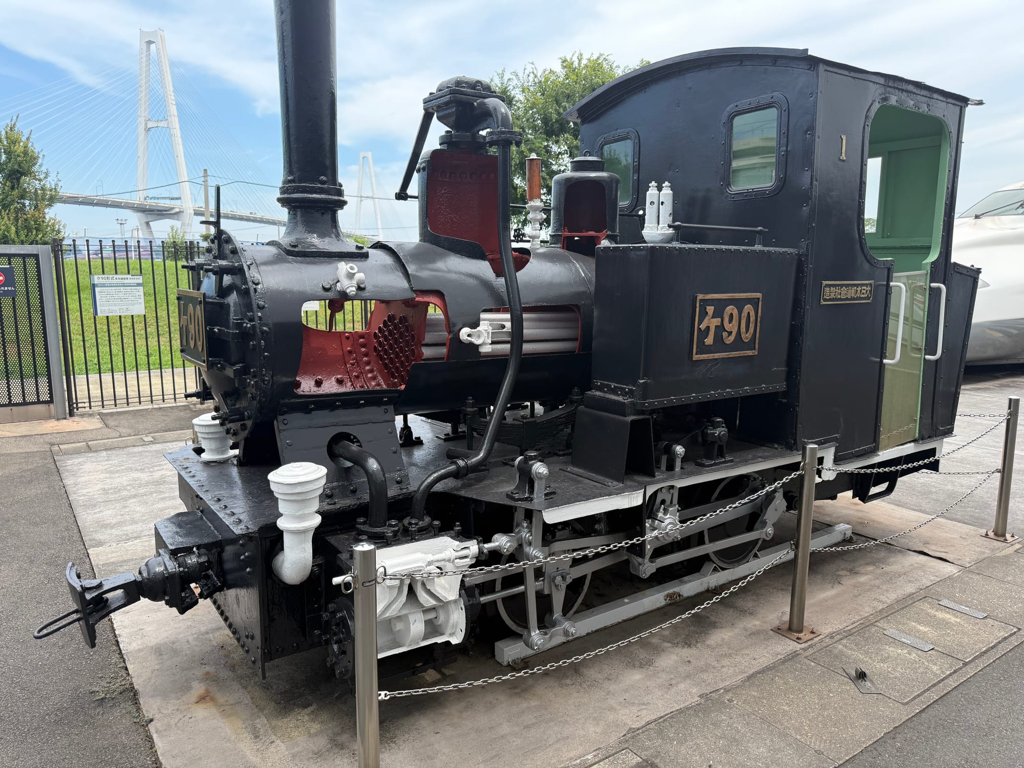 Cutaway steam locomotive displayed outside the SCMAGLEV and Railway Park in Nagoya, revealing its internal boiler and mechanical components, with the Isewangan Expressway bridge in the background.
