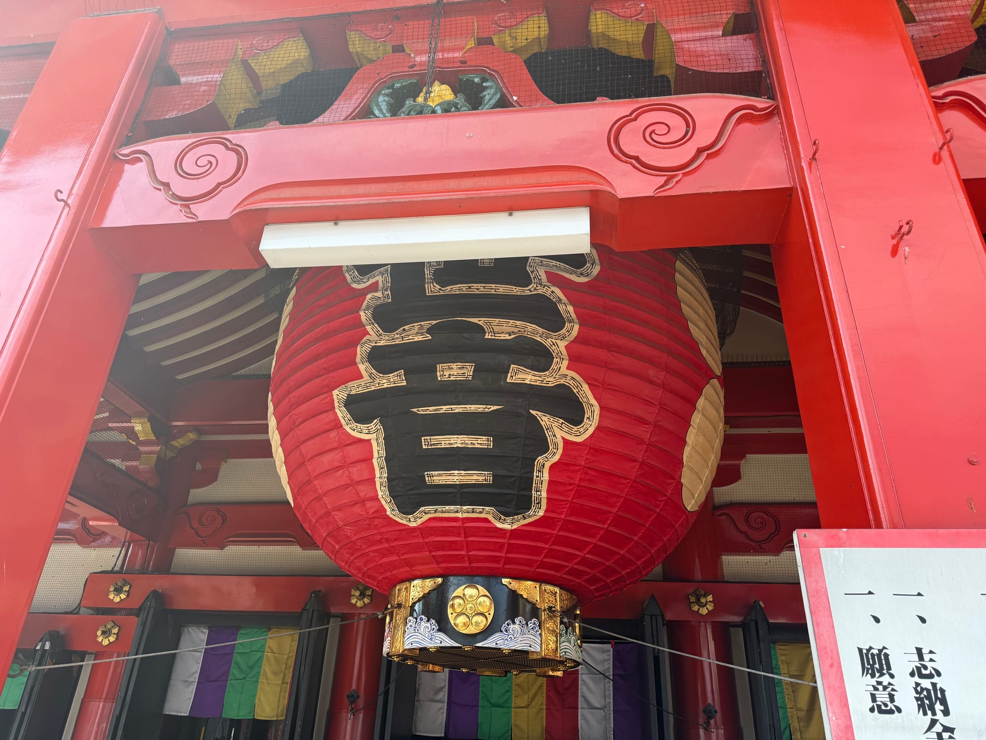 Large red paper lantern hanging at the entrance of Ōsu Kannon Temple in Nagoya, framed by vibrant red wooden architecture and traditional Buddhist decorative features.
