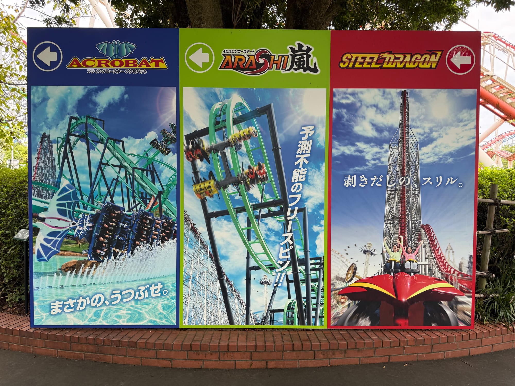 Promotional display at Nagashima Spa Land featuring Acrobat, Arashi and Steel Dragon 2000, with large photographs of the roller coasters and directional arrows.