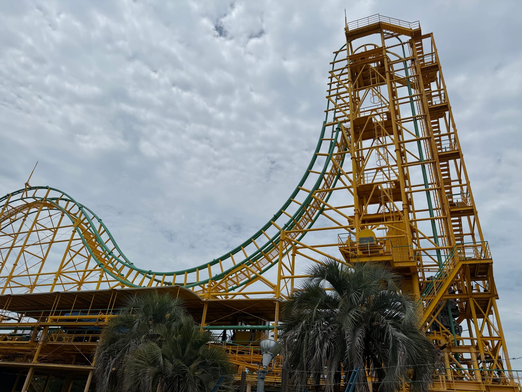 Ultra Twister roller coaster at Nagashima Spa Land, featuring its distinctive vertical lift, steep drop and bright yellow support structure beneath dramatic cloudy skies.