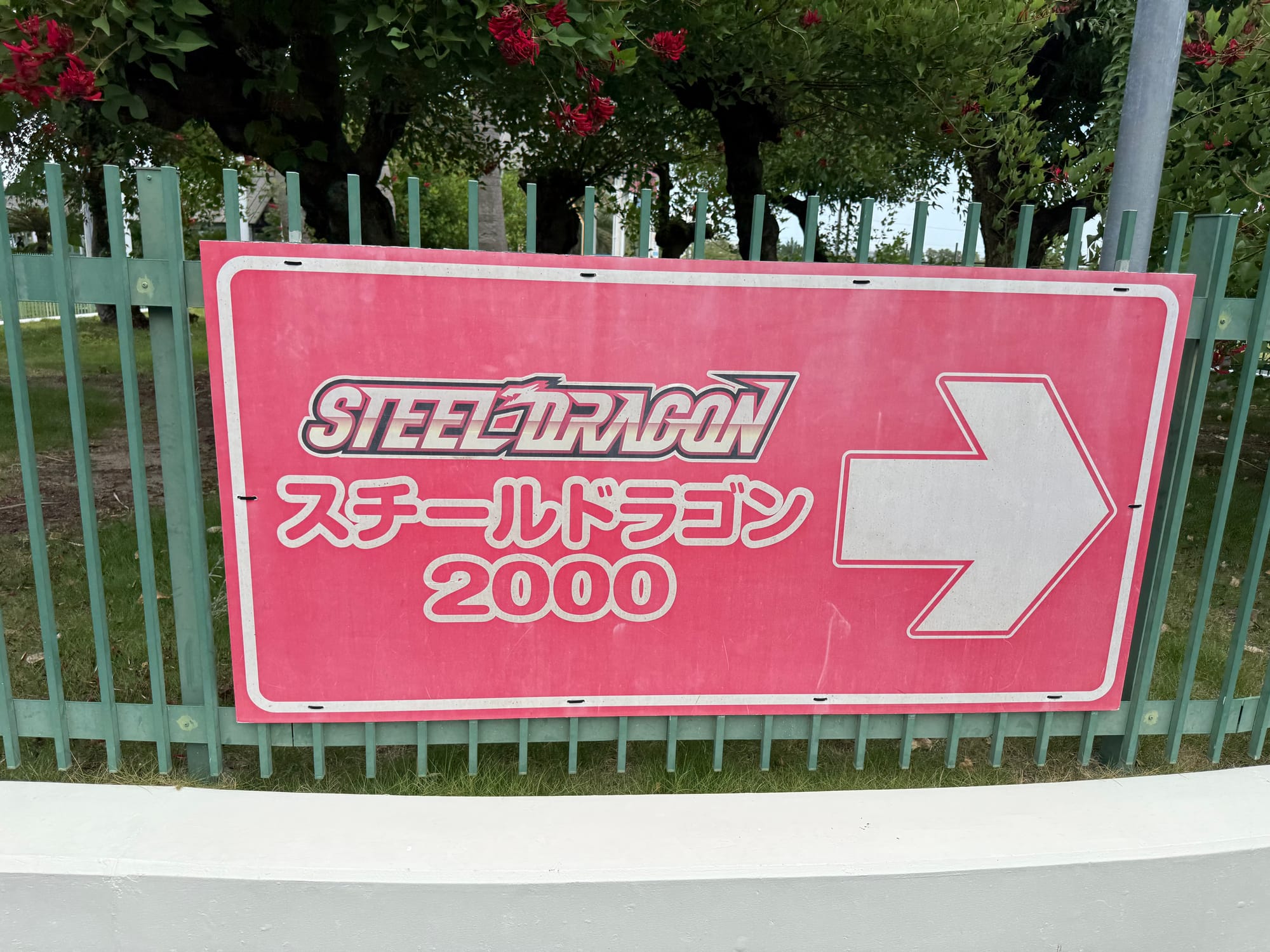 Sign for Steel Dragon 2000 at Nagashima Spa Land, featuring the roller coaster's logo, Japanese text and a directional arrow pointing towards the attraction.