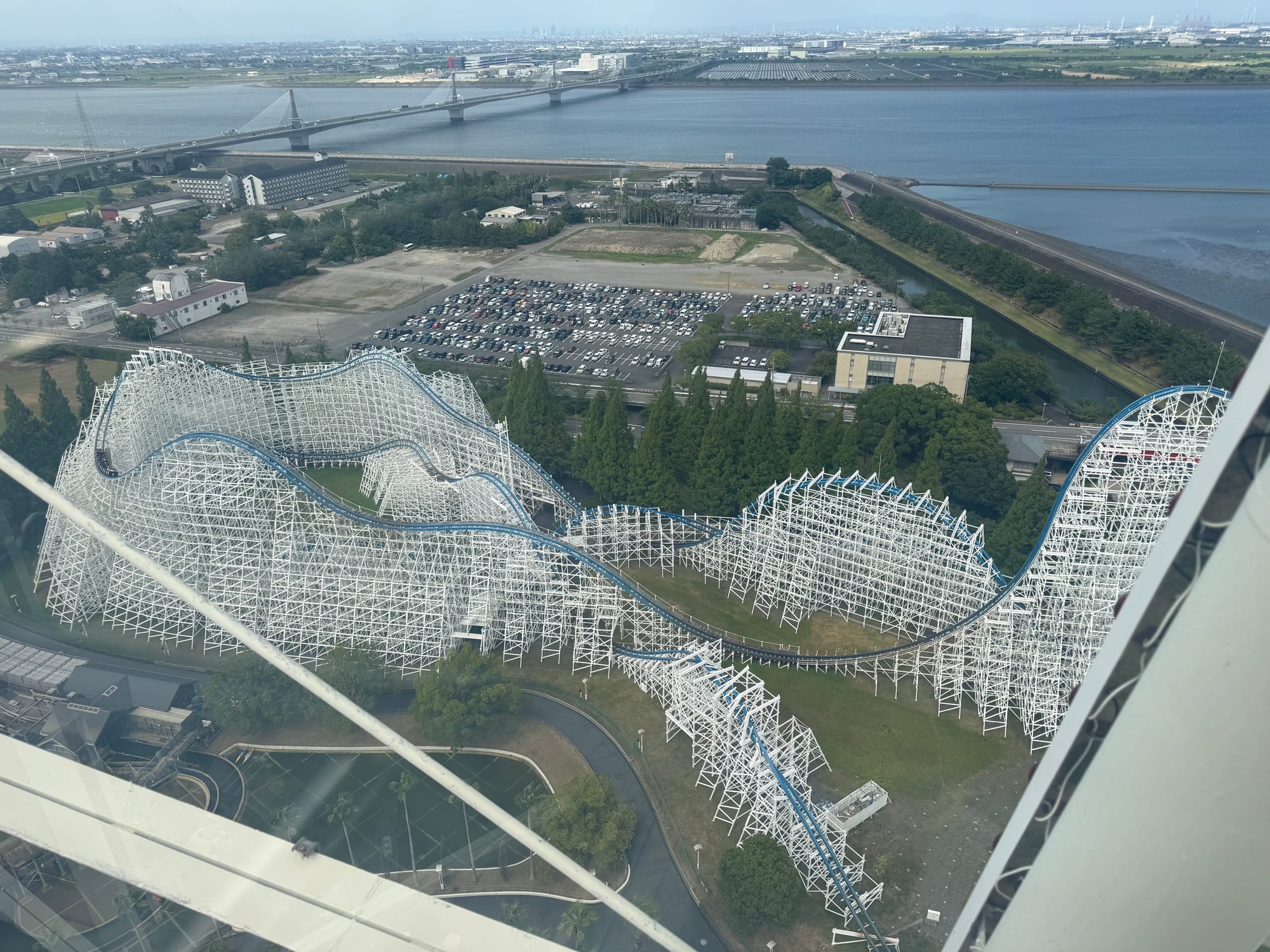 View from the Ferris wheel at Nagashima Spa Land overlooking the White Cyclone wooden roller coaster, with its vast white structure beside rivers, bridges and surrounding countryside.