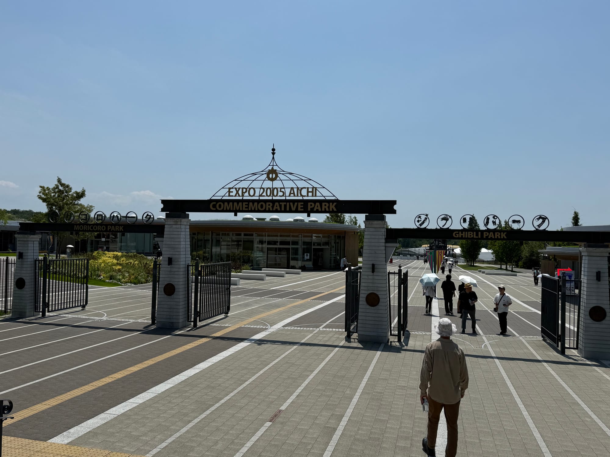 Entrance to Expo 2005 Aichi Commemorative Park and Ghibli Park, with visitors walking through the gates beneath signs for Moricoro Park and Ghibli Park on a sunny day.