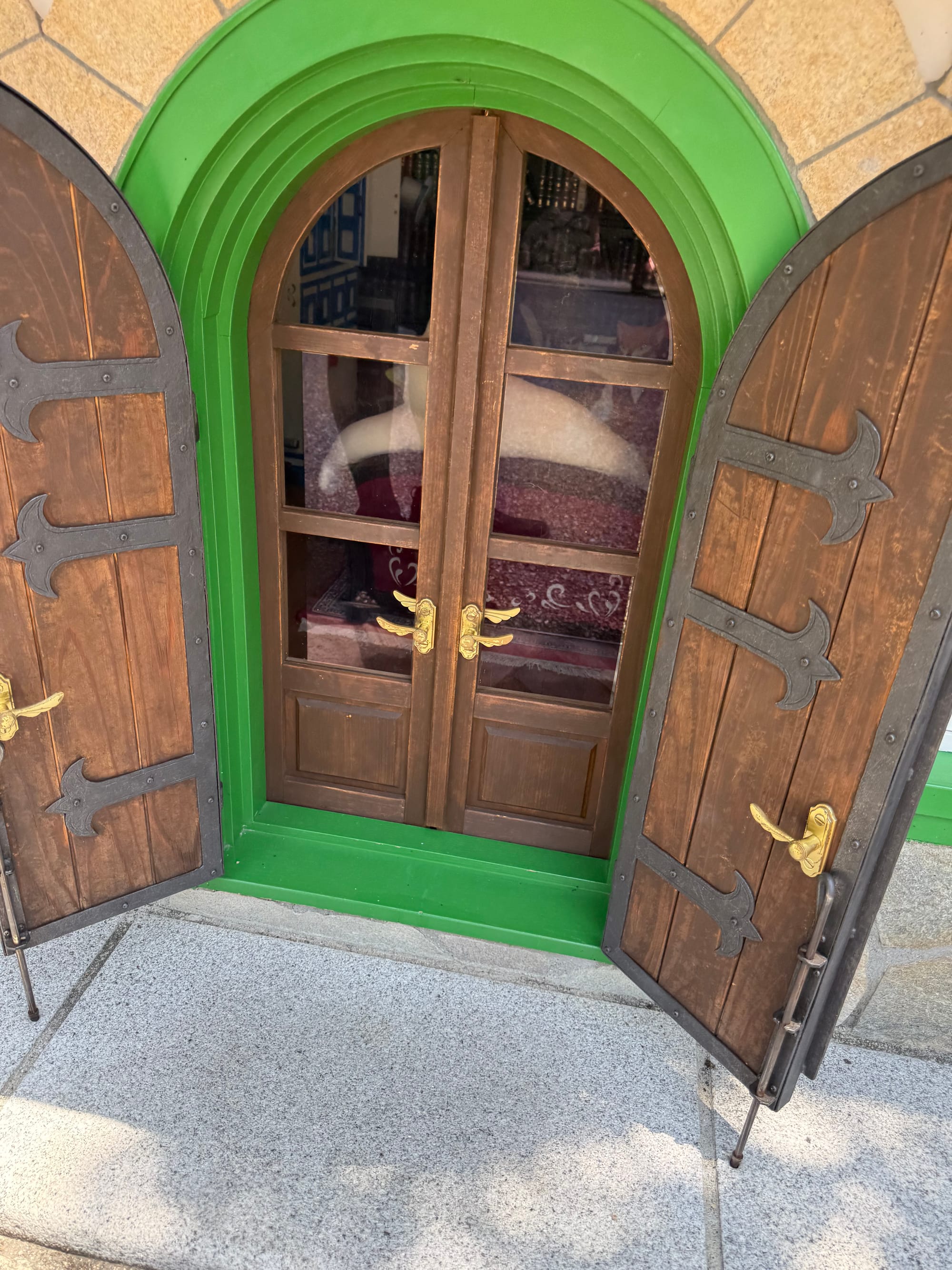 Entrance to the Cat Bureau at Ghibli Park, featuring small green-trimmed doors opened to reveal a glimpse of the giant cat furnishings inside the whimsical building.