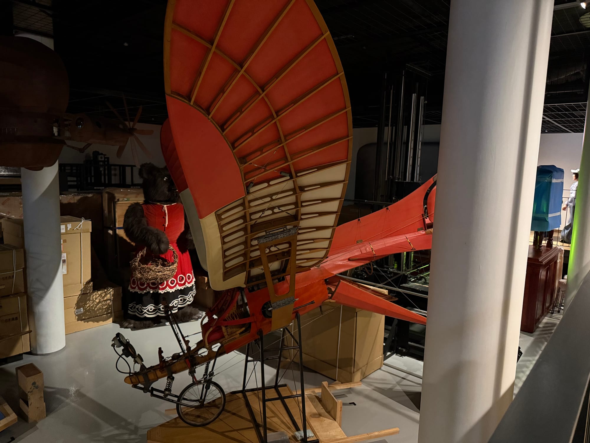Red-winged flying machine display inside Ghibli Park's Grand Warehouse, inspired by Studio Ghibli's fantastical aviation designs and surrounded by props from various films.