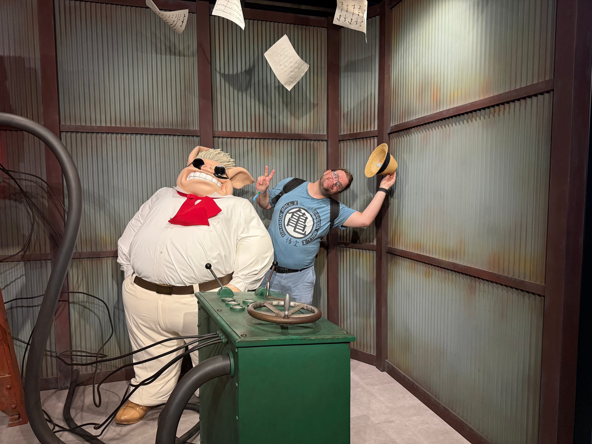 Visitor poses beside a model of Marco Pagot from Porco Rosso in the Becoming Characters in Memorable Ghibli Scenes exhibit, with airship controls and flying papers around the display.