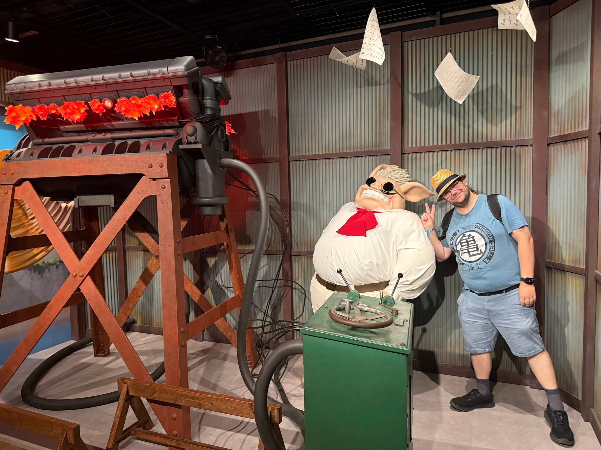 Visitor poses beside Marco Pagot from Porco Rosso in the Becoming Characters in Memorable Ghibli Scenes exhibit, with airship machinery, controls and flying papers around the display.