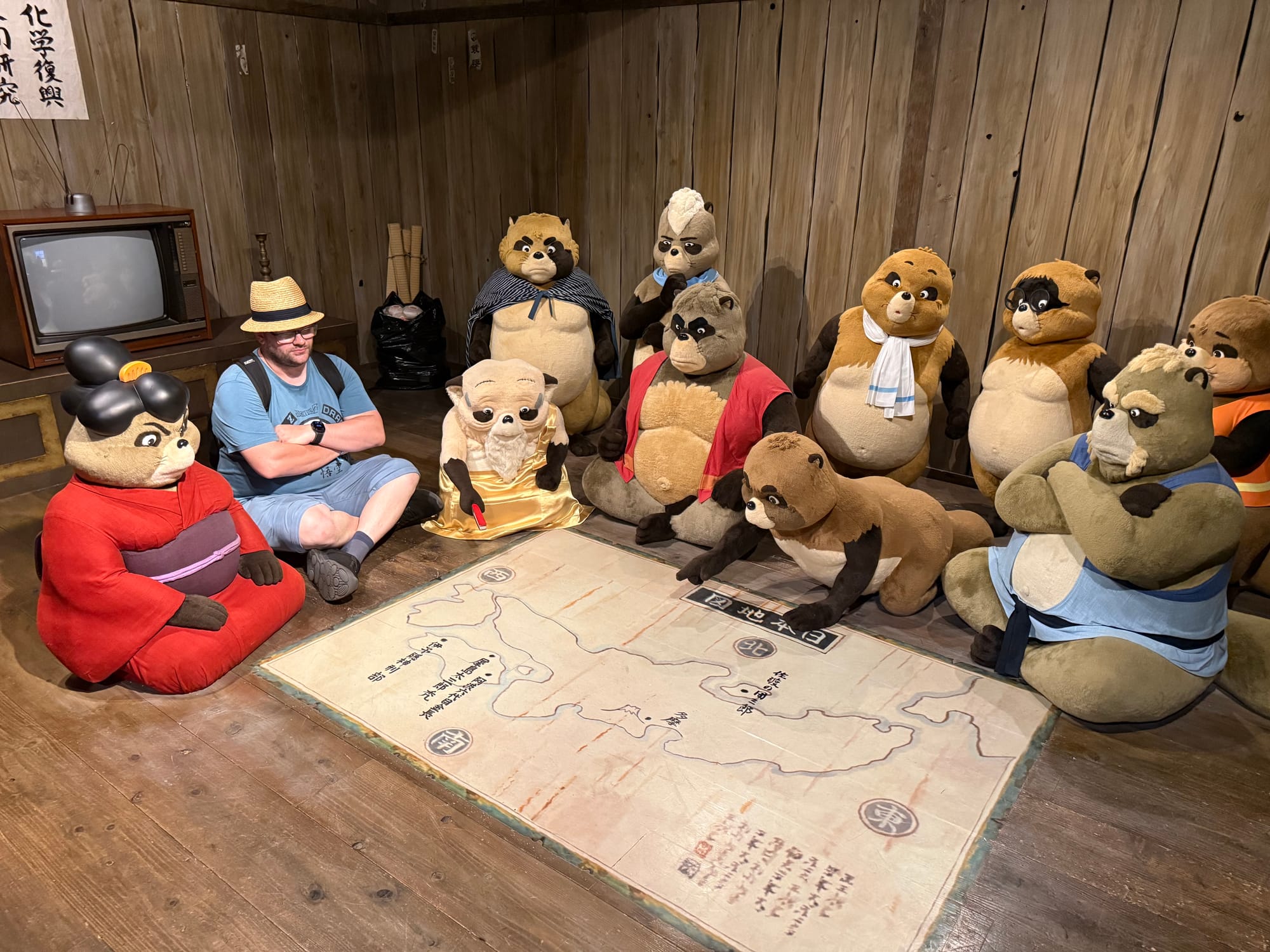 Visitor sits among tanuki characters around a map in the Becoming Characters in Memorable Ghibli Scenes exhibit, recreating a scene from Pom Poko inside Ghibli Park.