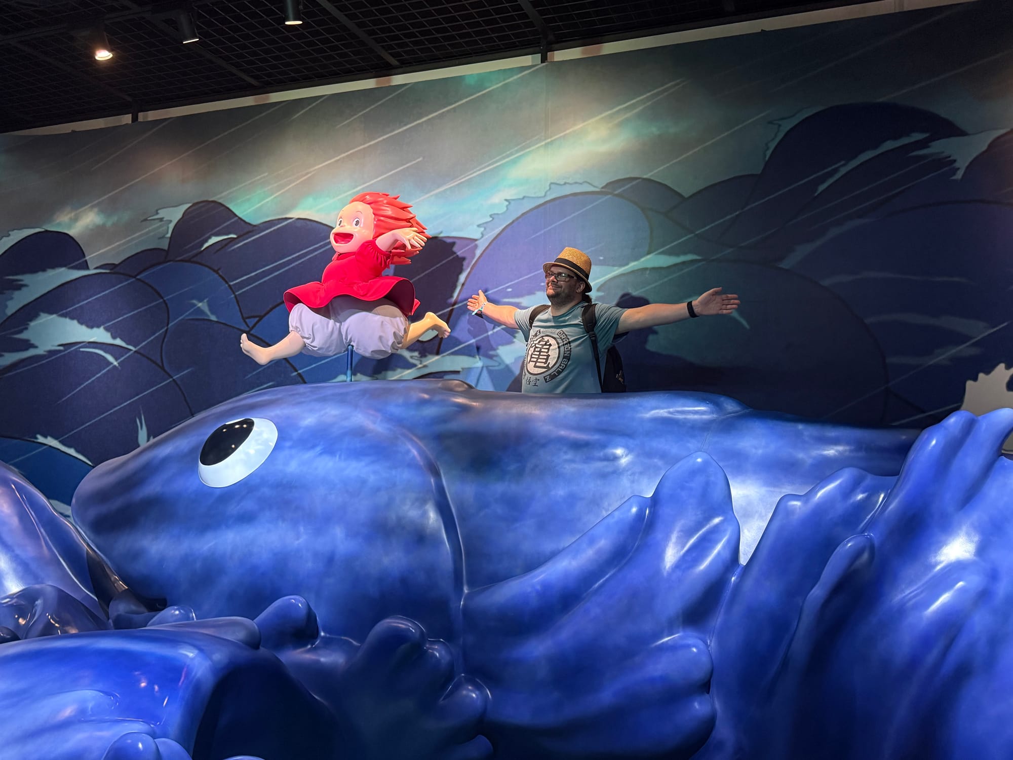 Visitor stands beside Ponyo on a giant blue fish in the Becoming Characters in Memorable Ghibli Scenes exhibit, recreating a scene from Ponyo amid stormy seas.