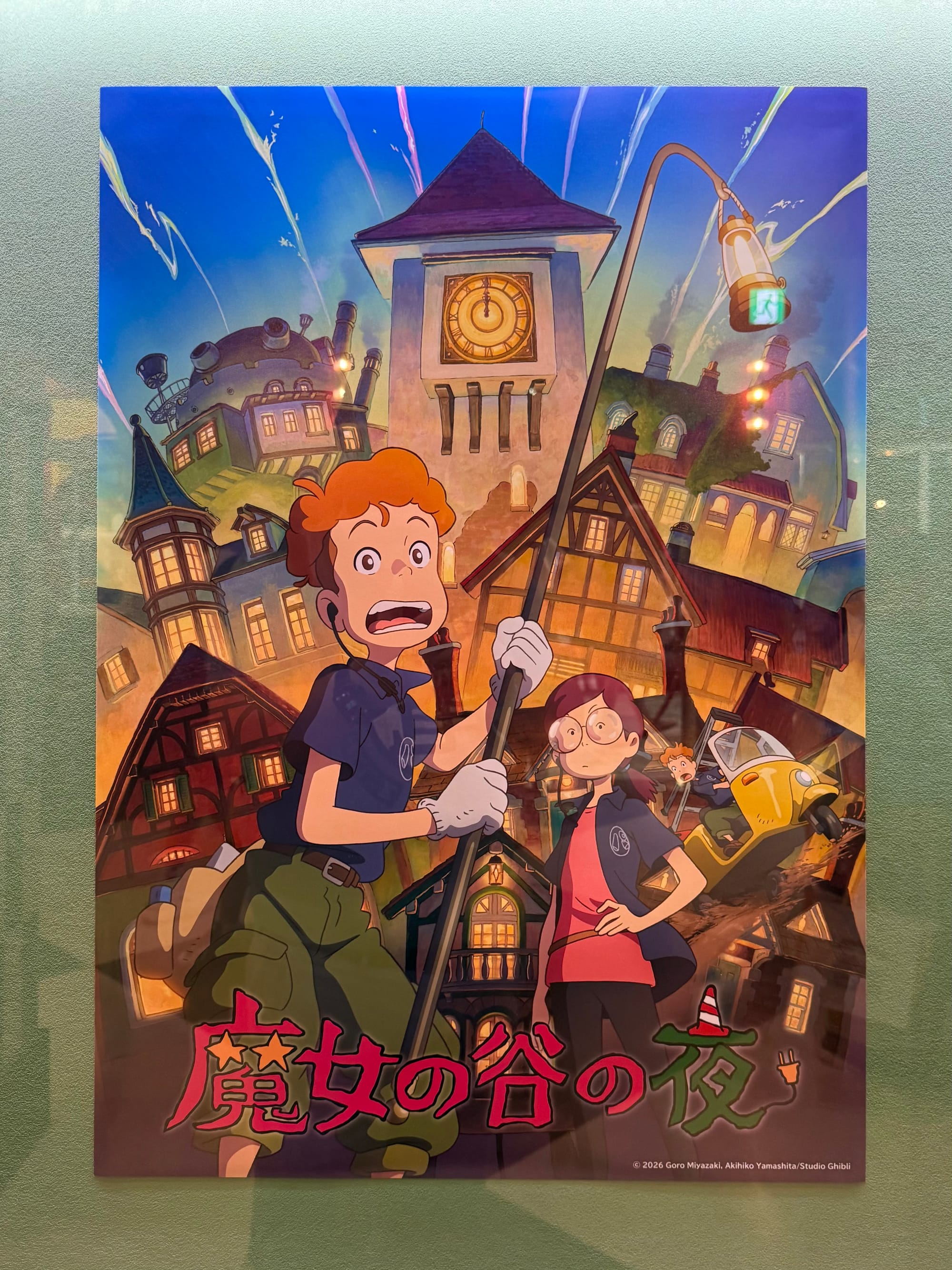 Poster for A Night in the Valley of the Witches displayed at Ghibli Park's Grand Warehouse, featuring characters exploring a magical town beneath a prominent clock tower.