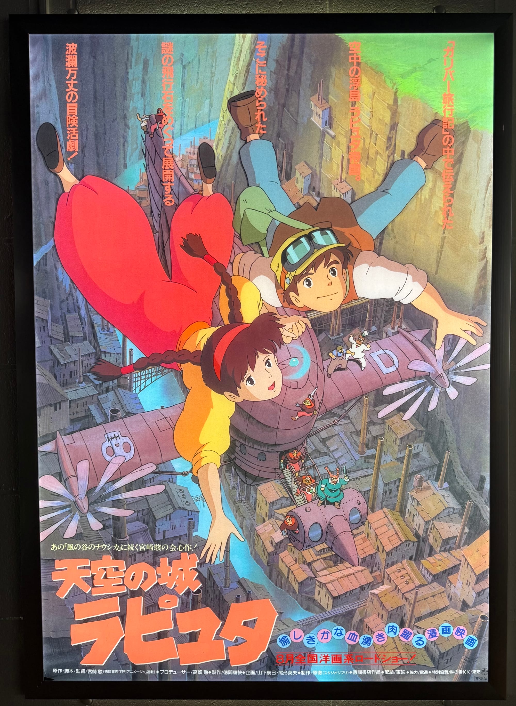 Poster for Castle in the Sky displayed at Ghibli Park's Grand Warehouse, showing Pazu and Sheeta flying above a vast industrial mining town in a deep canyon.
