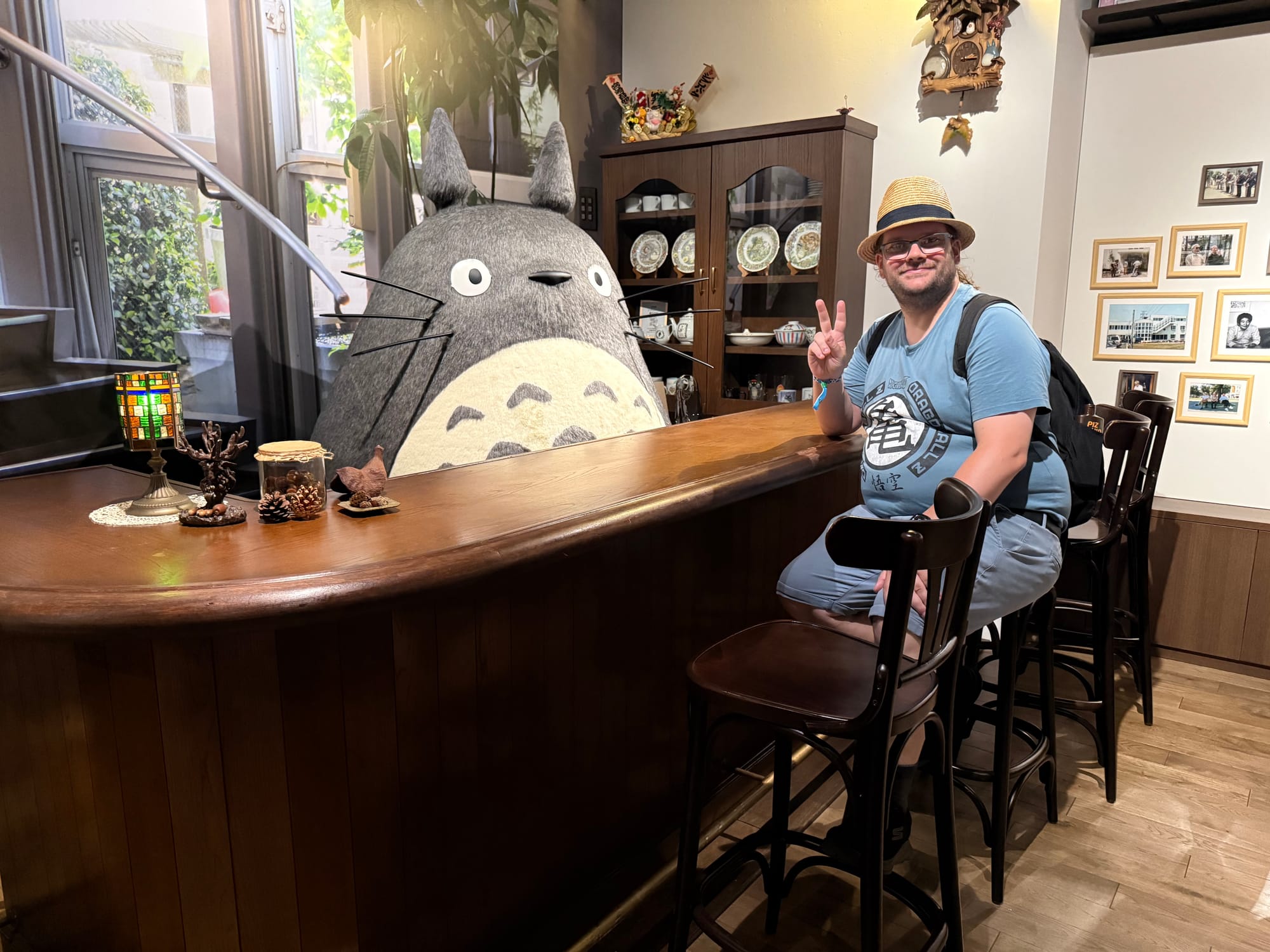 Visitor sits at a wooden bar beside a life-sized Totoro display inside Ghibli Park's Grand Warehouse, recreating the atmosphere of a cosy Studio Ghibli-inspired interior.
