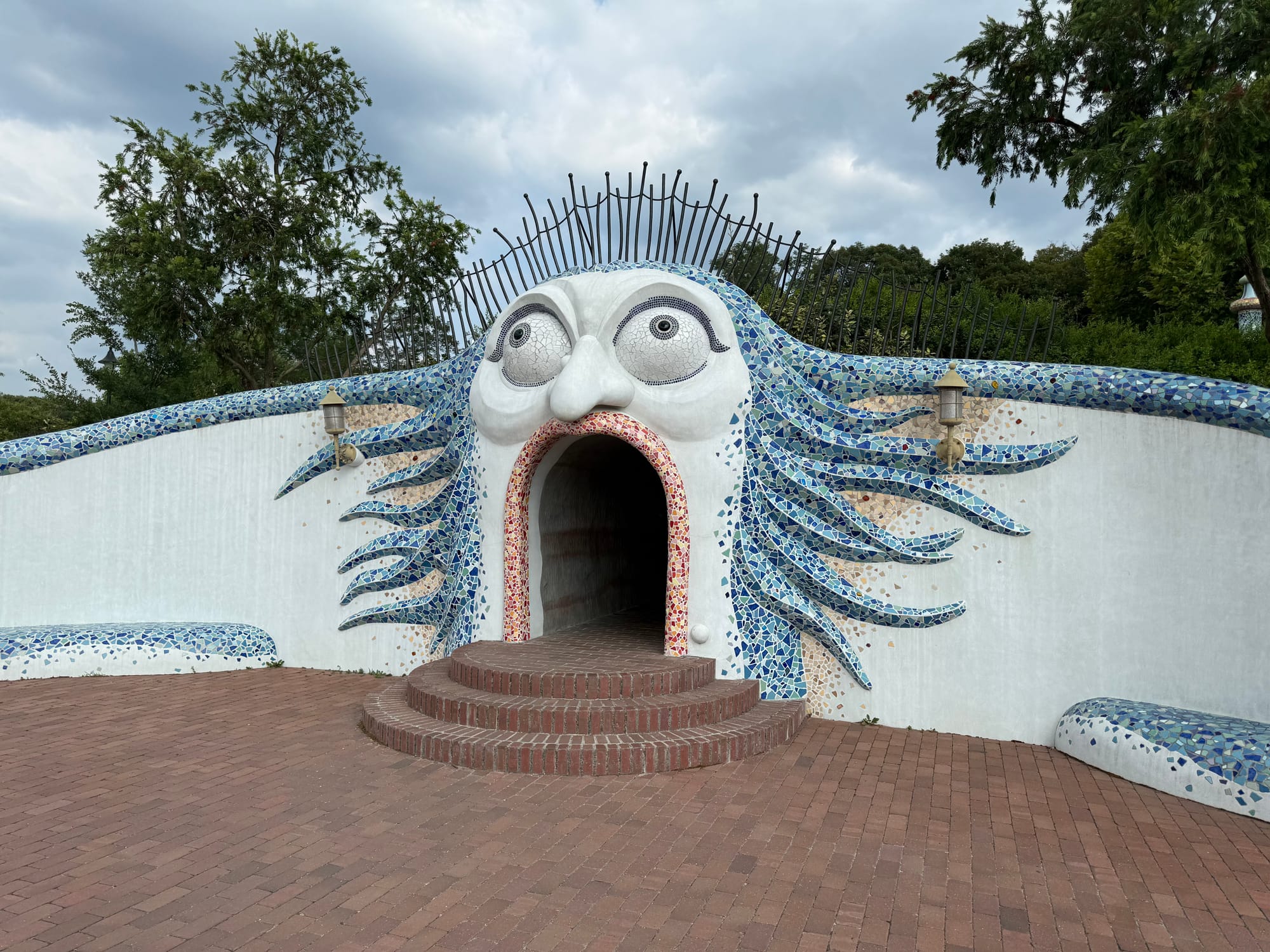 Witch House entrance at Ghibli Park's Valley of Witches, featuring a mosaic face with flowing blue hair, wide eyes and an arched doorway forming an open mouth.
