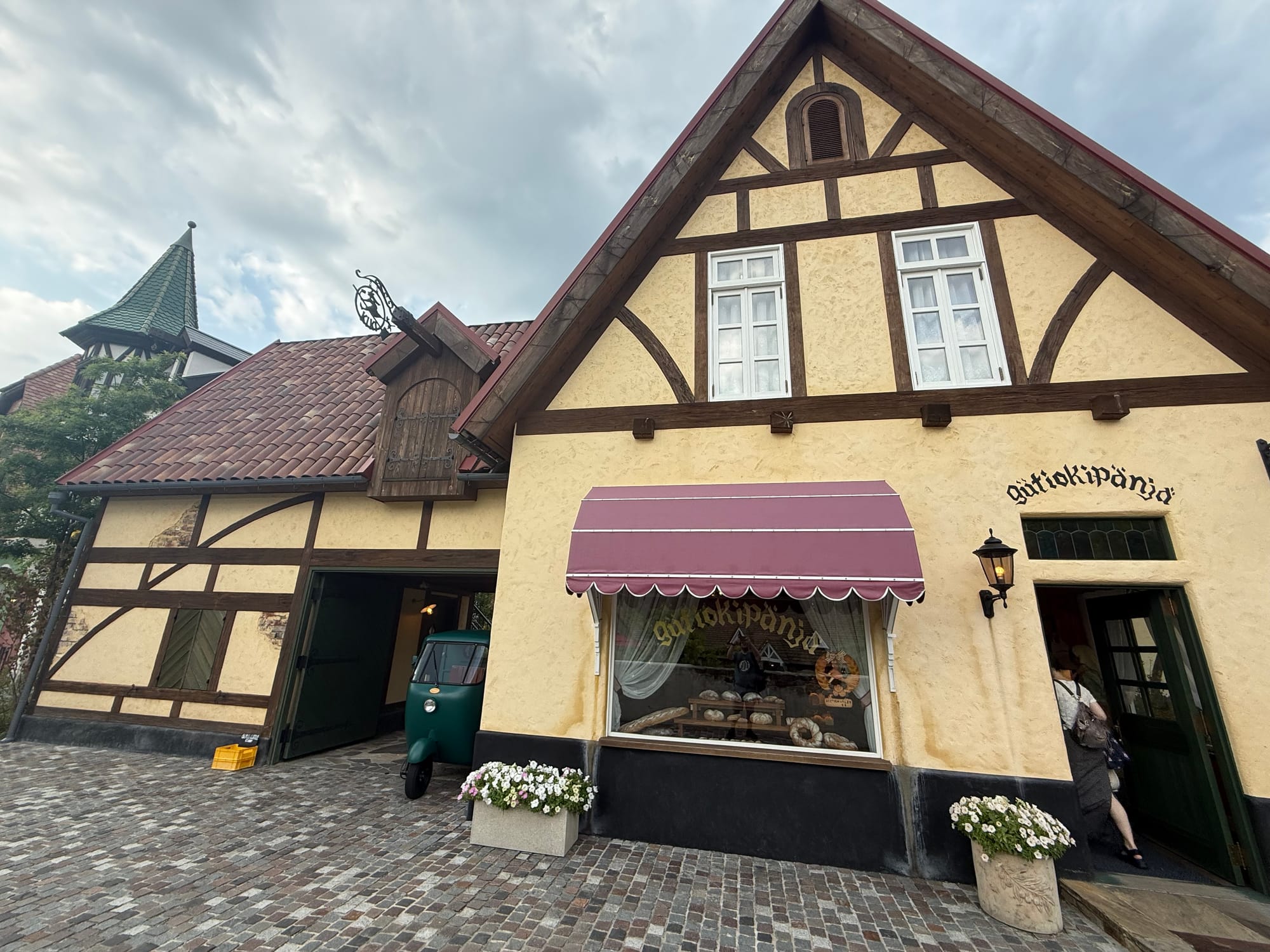 Gütiokipänjä Bakery from Kiki's Delivery Service at Ghibli Park's Valley of Witches, featuring the bakery shopfront, delivery vehicle and half-timbered architecture.