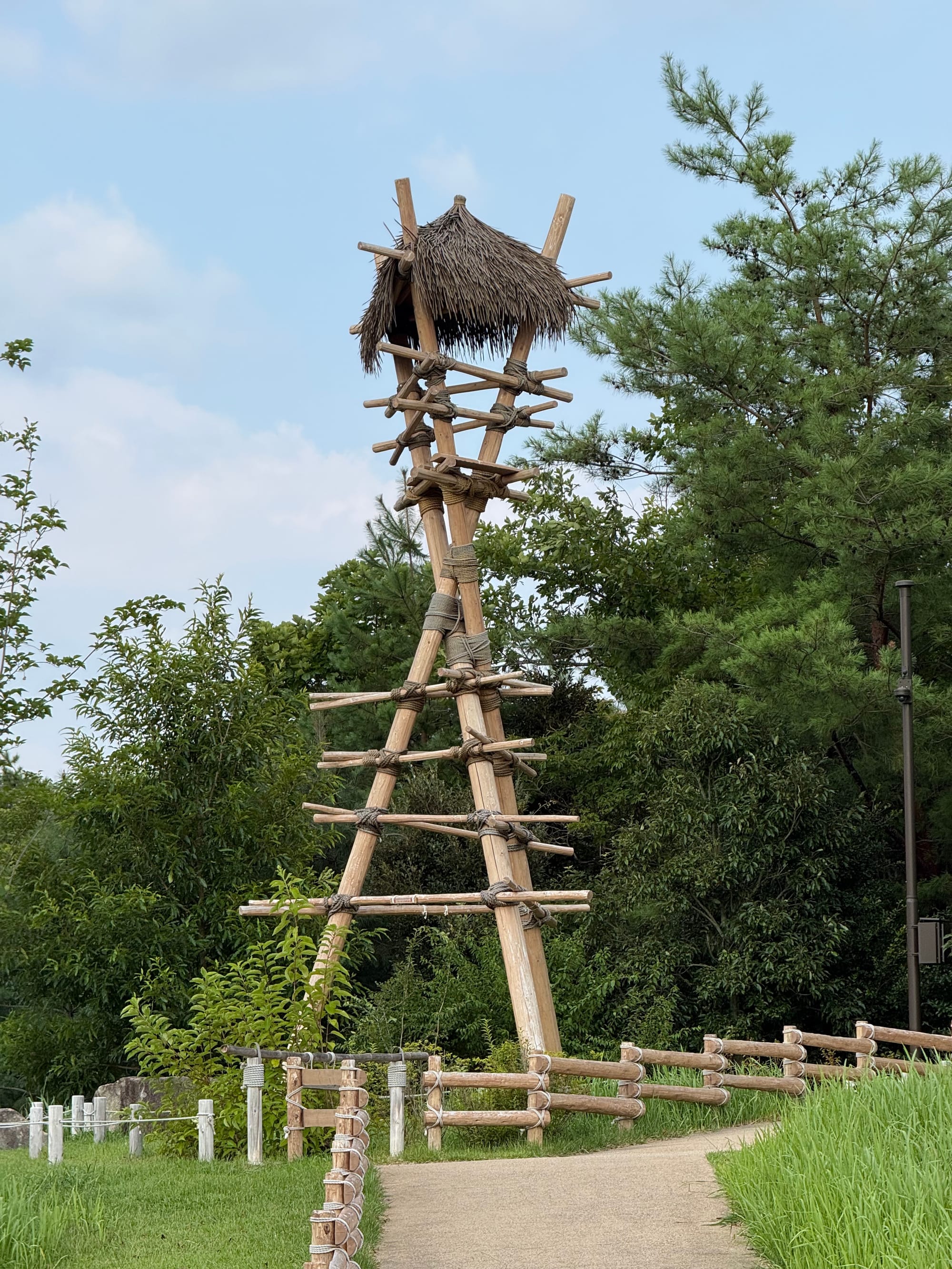 Watchtower from Princess Mononoke at Ghibli Park, featuring a tall wooden structure with a thatched roof, rope bindings and a surrounding grassland setting.
