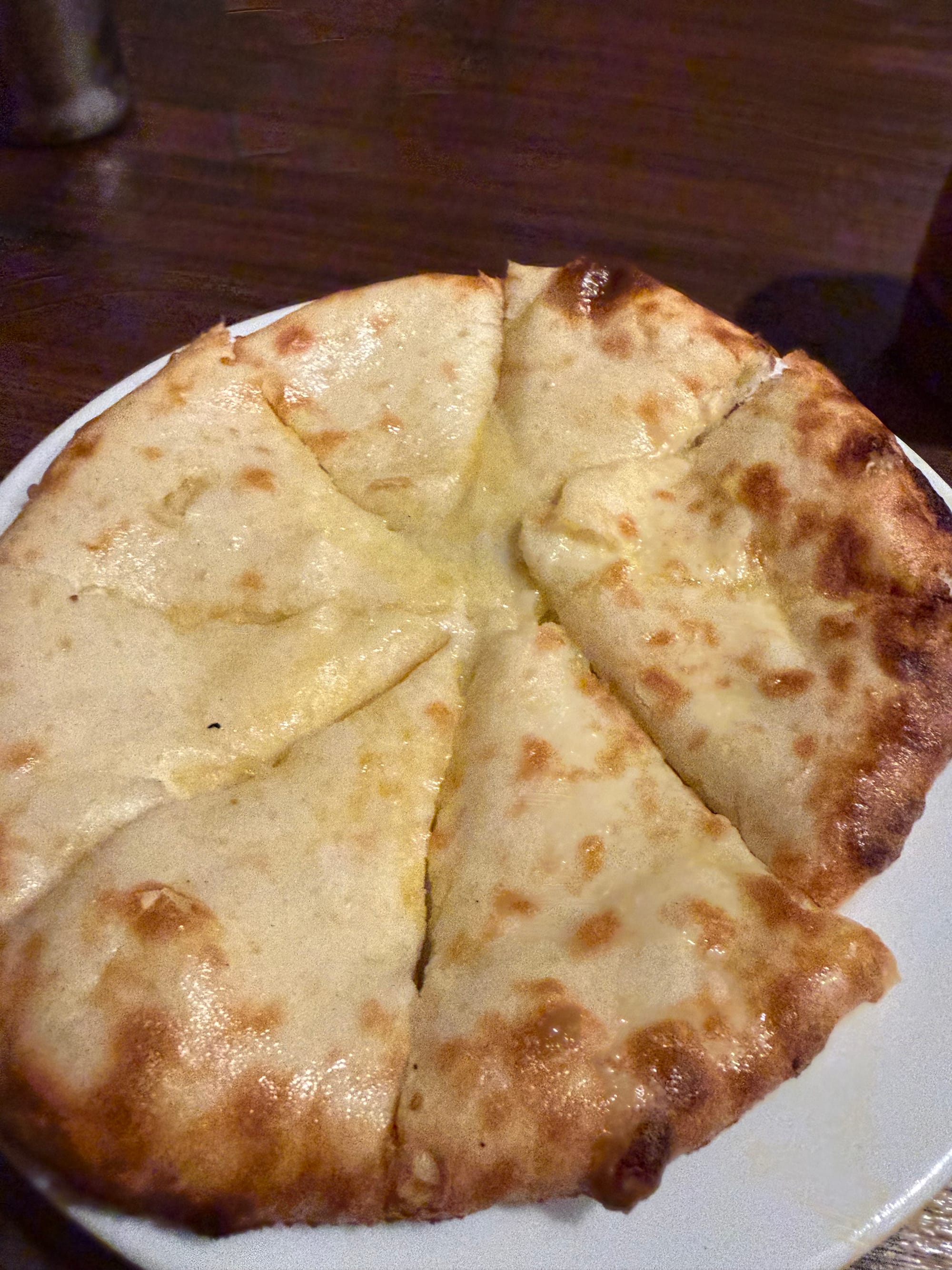 Cheese naan bread served on a white plate, cut into slices with melted cheese visible between the layers of freshly baked naan.