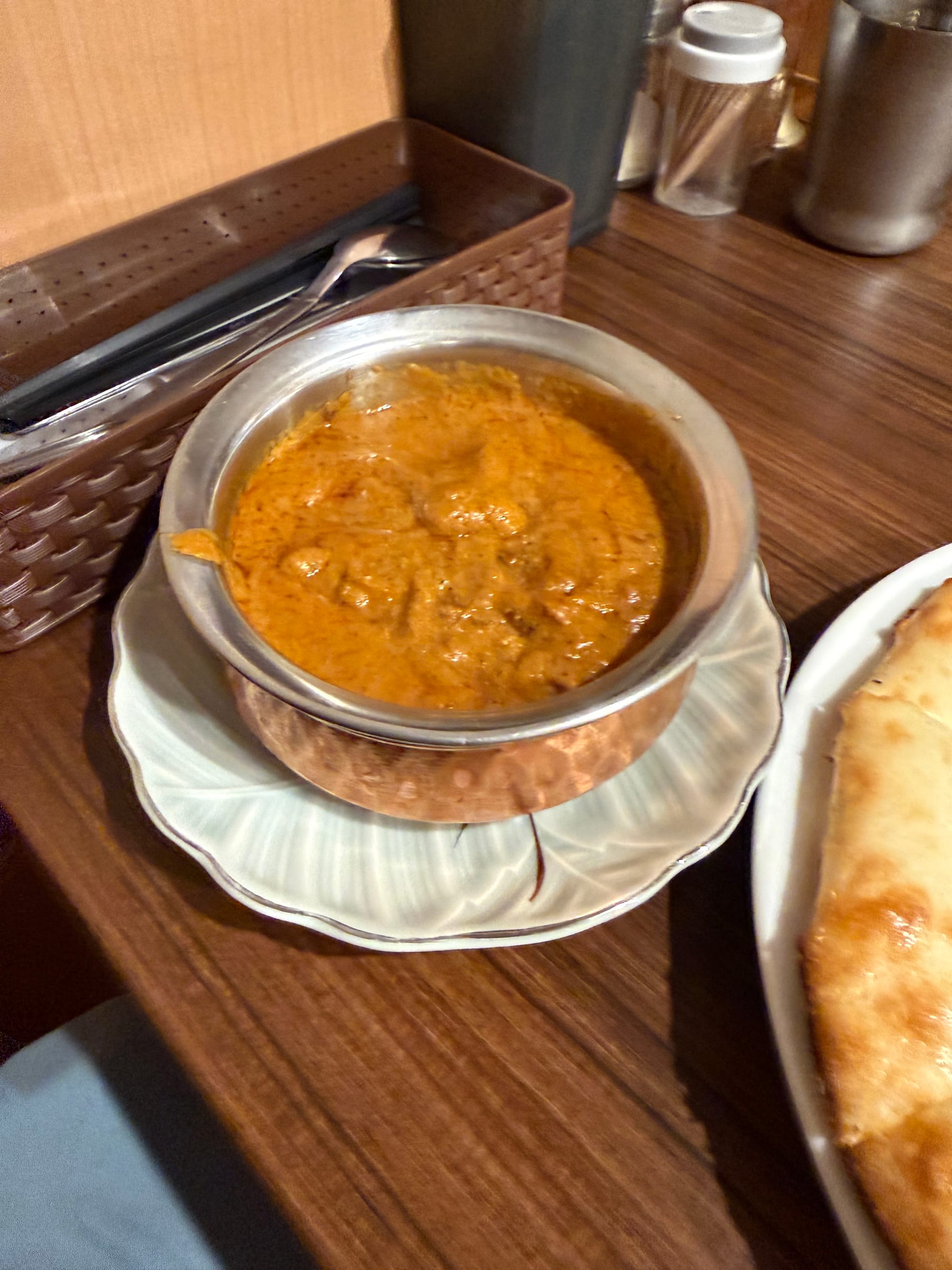 Bowl of chicken tikka masala served in a traditional metal dish at Baje Restaurant in Nagoya, featuring tender chicken pieces in a rich, creamy tomato-based curry sauce.
