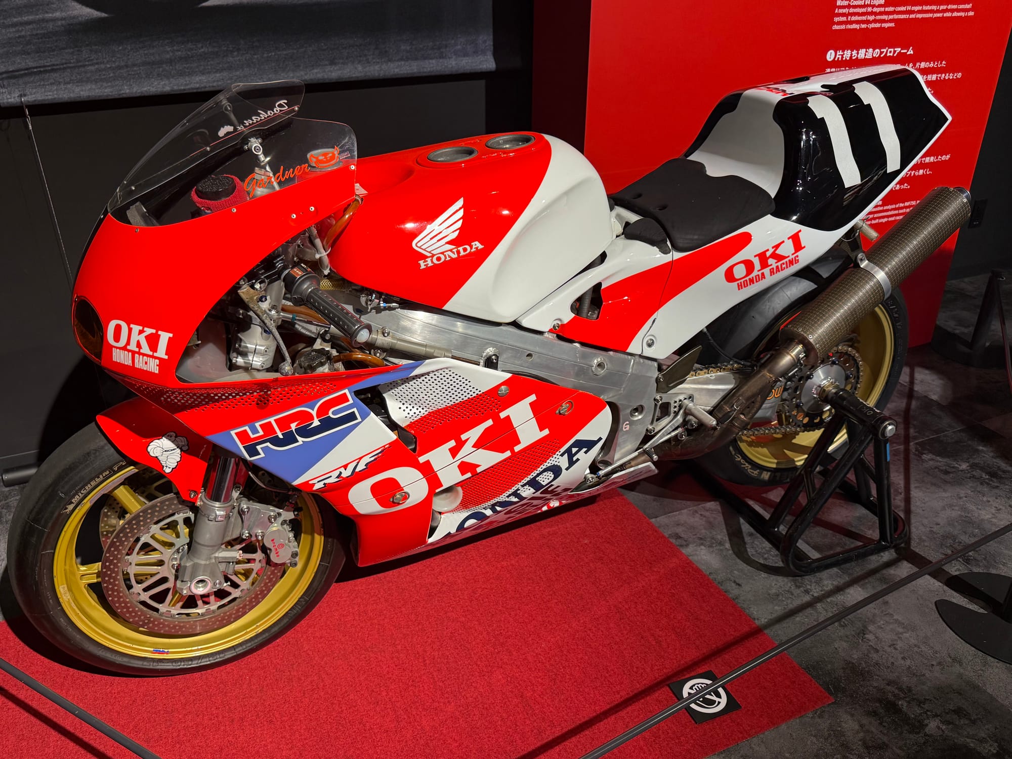 Honda RVF endurance racing motorcycle displayed at the Honda Racing Gallery, featuring OKI Honda Racing sponsorship, HRC branding and the red, white and blue racing livery.