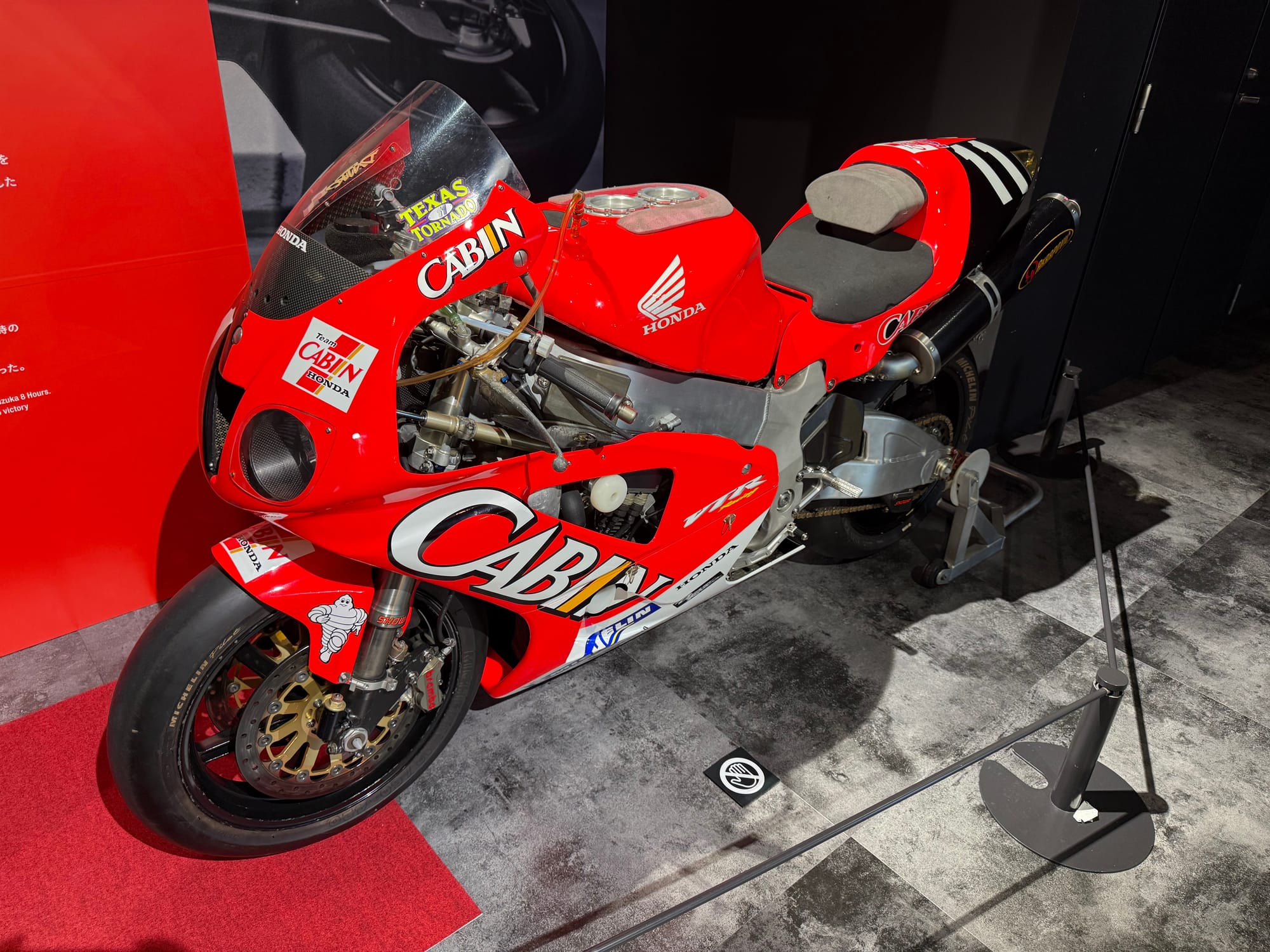 Honda VTR1000SPW endurance racing motorcycle displayed at the Honda Racing Gallery, featuring Cabin Honda sponsorship, a V-twin engine and red-and-white racing livery.