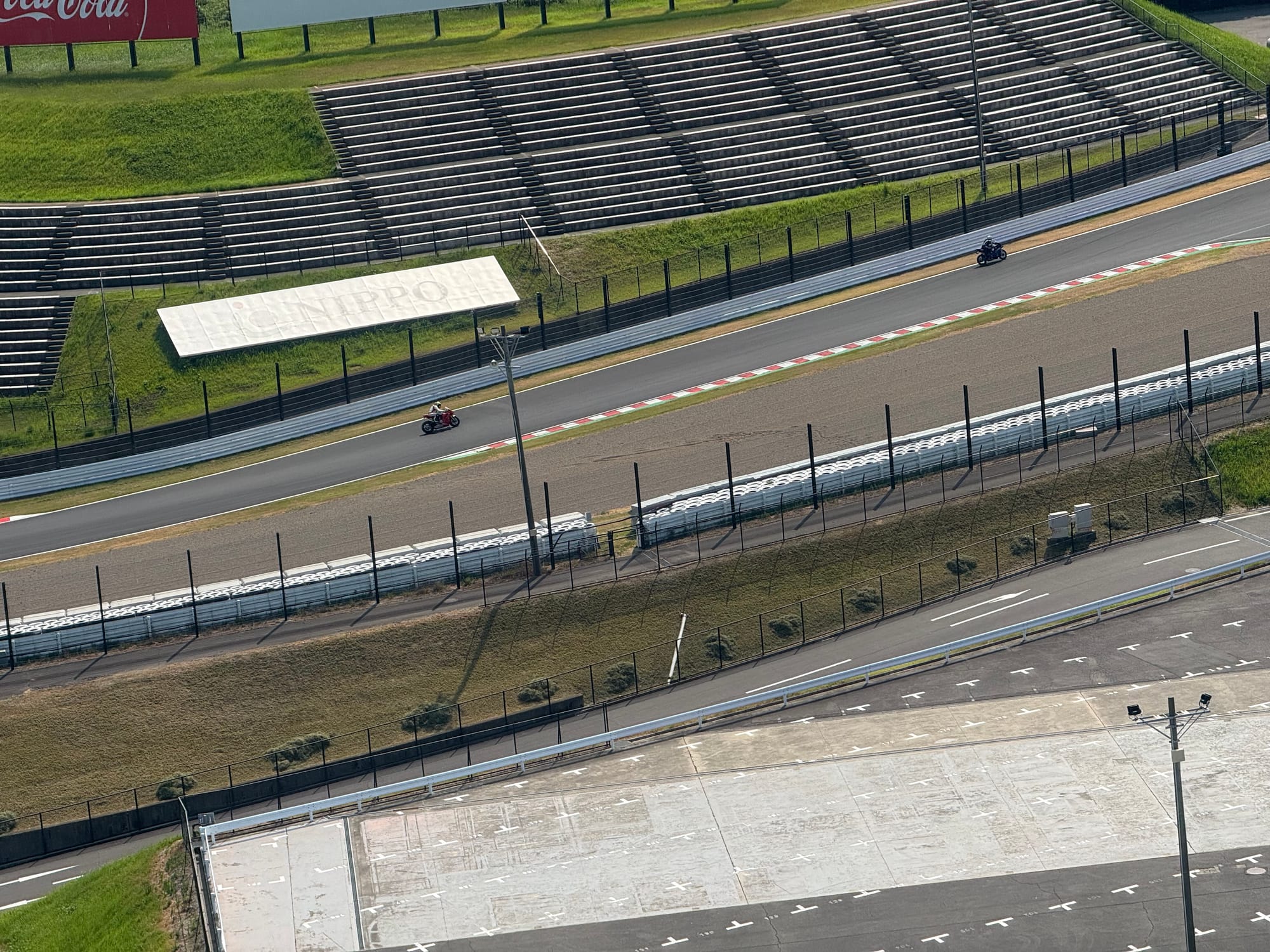 Motorcyclists ride along the Suzuka Circuit during a two-wheel practice session, passing the grandstands and heading into the pits on a section of the famous racing track.