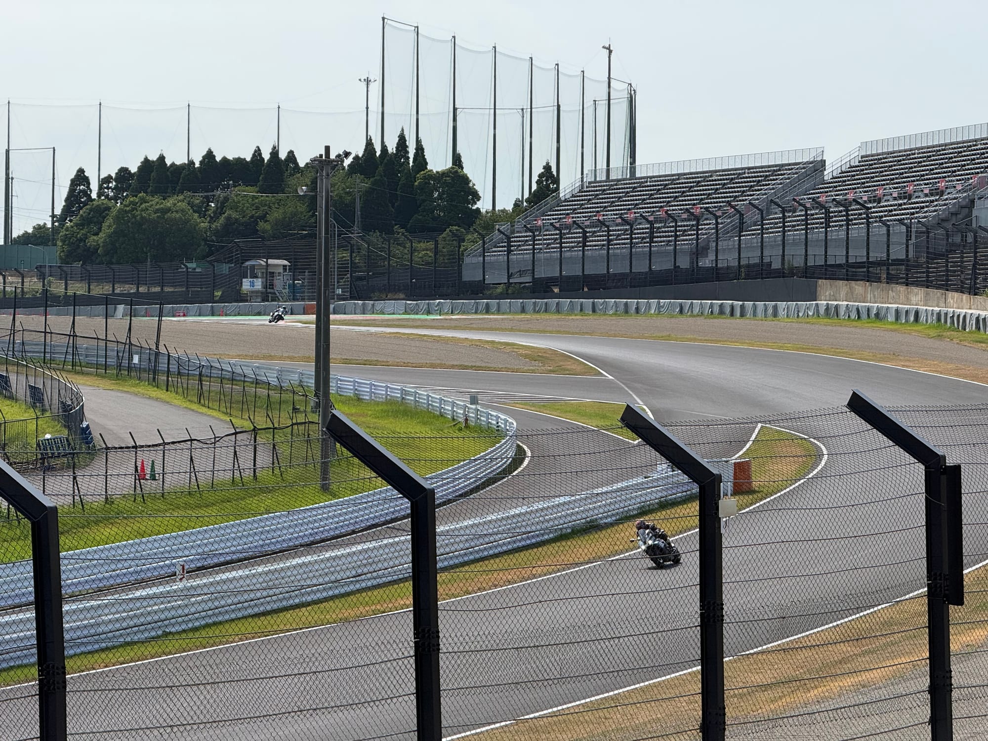 Motorcyclists lean through a corner during a two-wheel practice session at Suzuka Circuit, with grandstands, safety barriers and fencing surrounding the famous racing track.