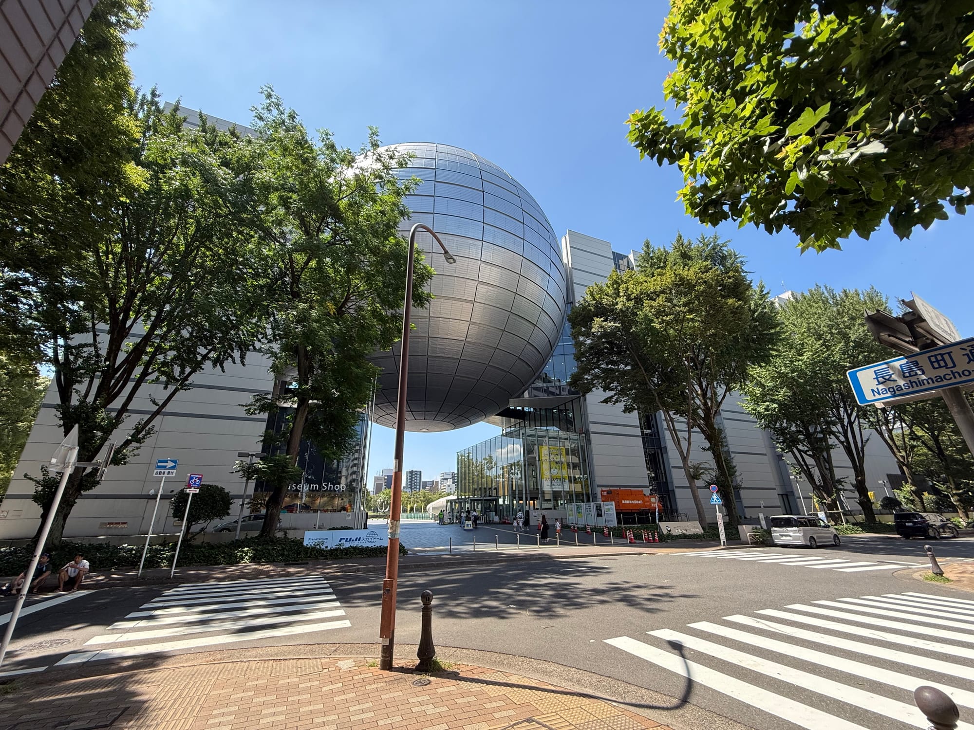 Nagoya City Science Museum viewed from across a street, featuring the large silver Fuji Sky Dome planetarium suspended between the museum's modern buildings.