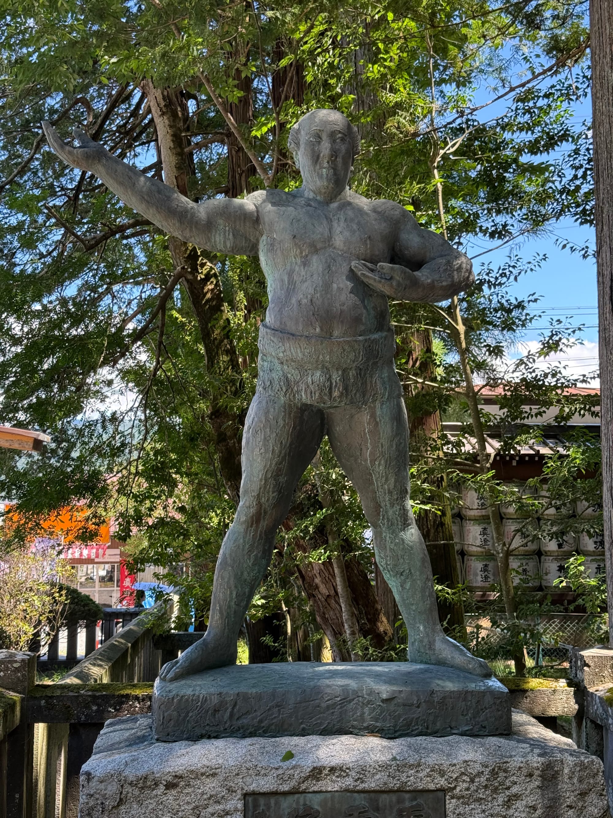 Bronze statue of Raiden Tameemon at Suwa Taisha Kamisha Honmiya, depicting the legendary Edo-period sumo wrestler in a traditional stance beneath towering cedar trees.