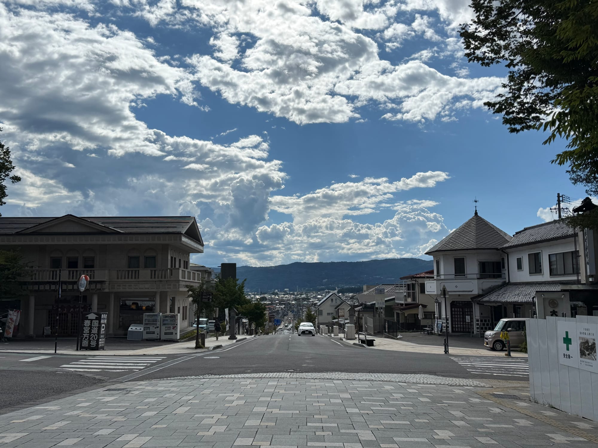 View from the torii gate of Suwa Taisha Shimosha Akimiya, looking down a straight street toward the town of Shimosuwa, with mountains and dramatic clouds in the distance.