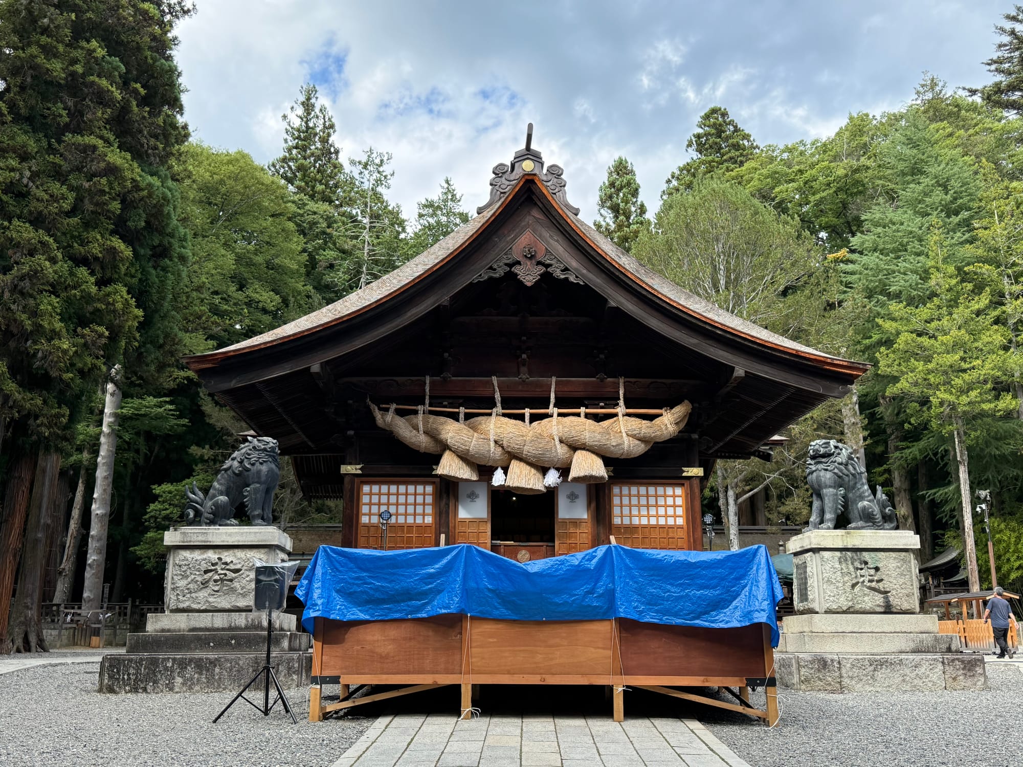 Main worship hall of Suwa Taisha Shimosha Akimiya, featuring a massive sacred shimenawa rope, guardian komainu statues and traditional wooden architecture.