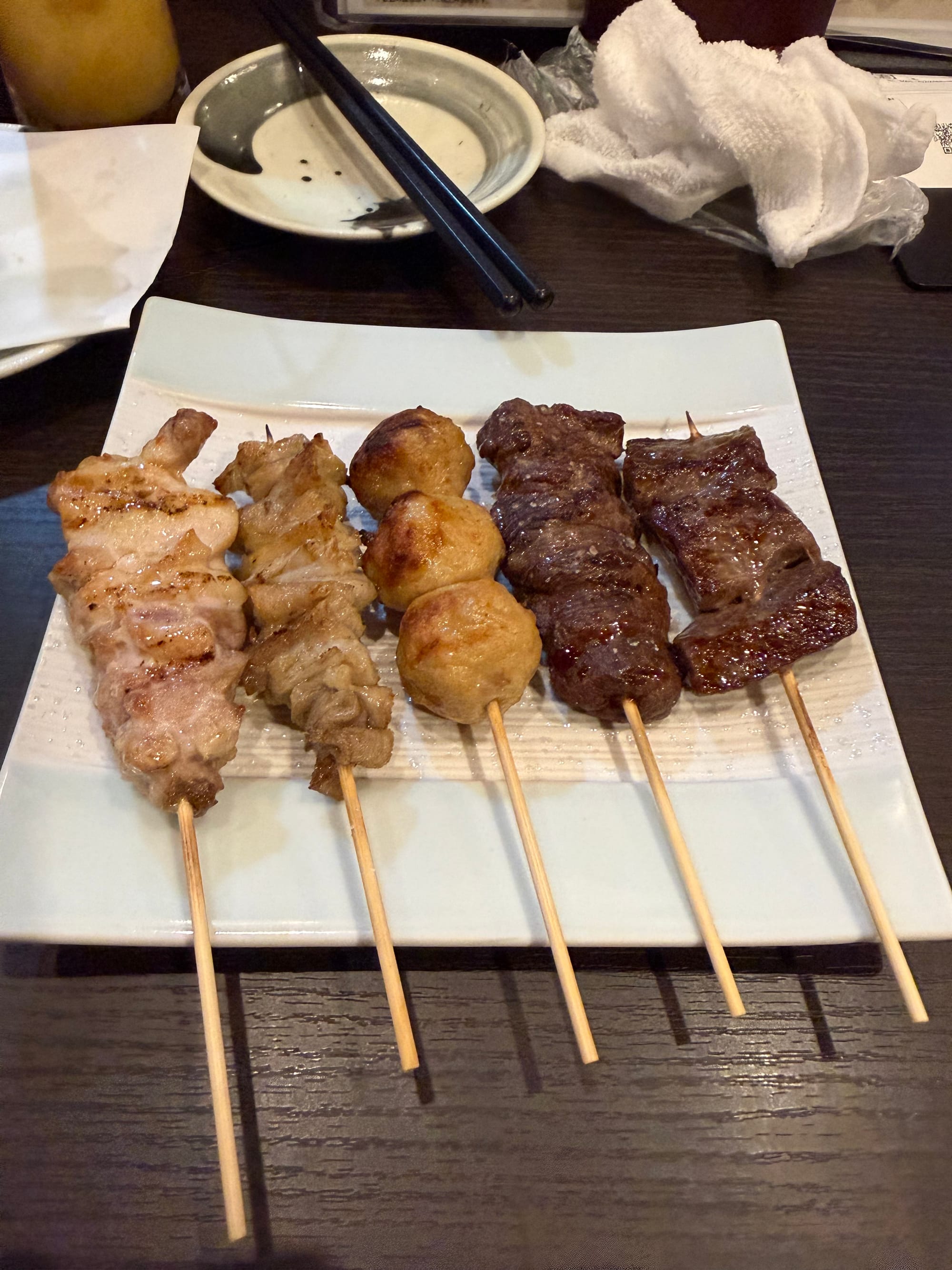 Plate of assorted grilled skewers from a Shinshu Welcome Set, featuring chicken, meatballs, venison and beef, served on a rectangular dish at a restaurant in Nagano Prefecture.