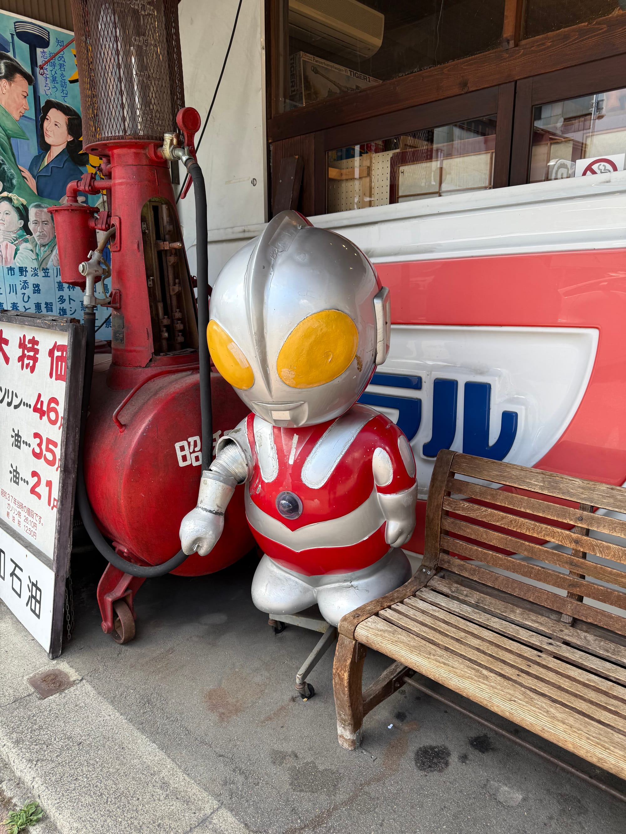Ultraman character statue outside the Takayama Showa-kan Museum, displayed beside a vintage petrol pump, retro signboards and a wooden bench at the museum entrance.