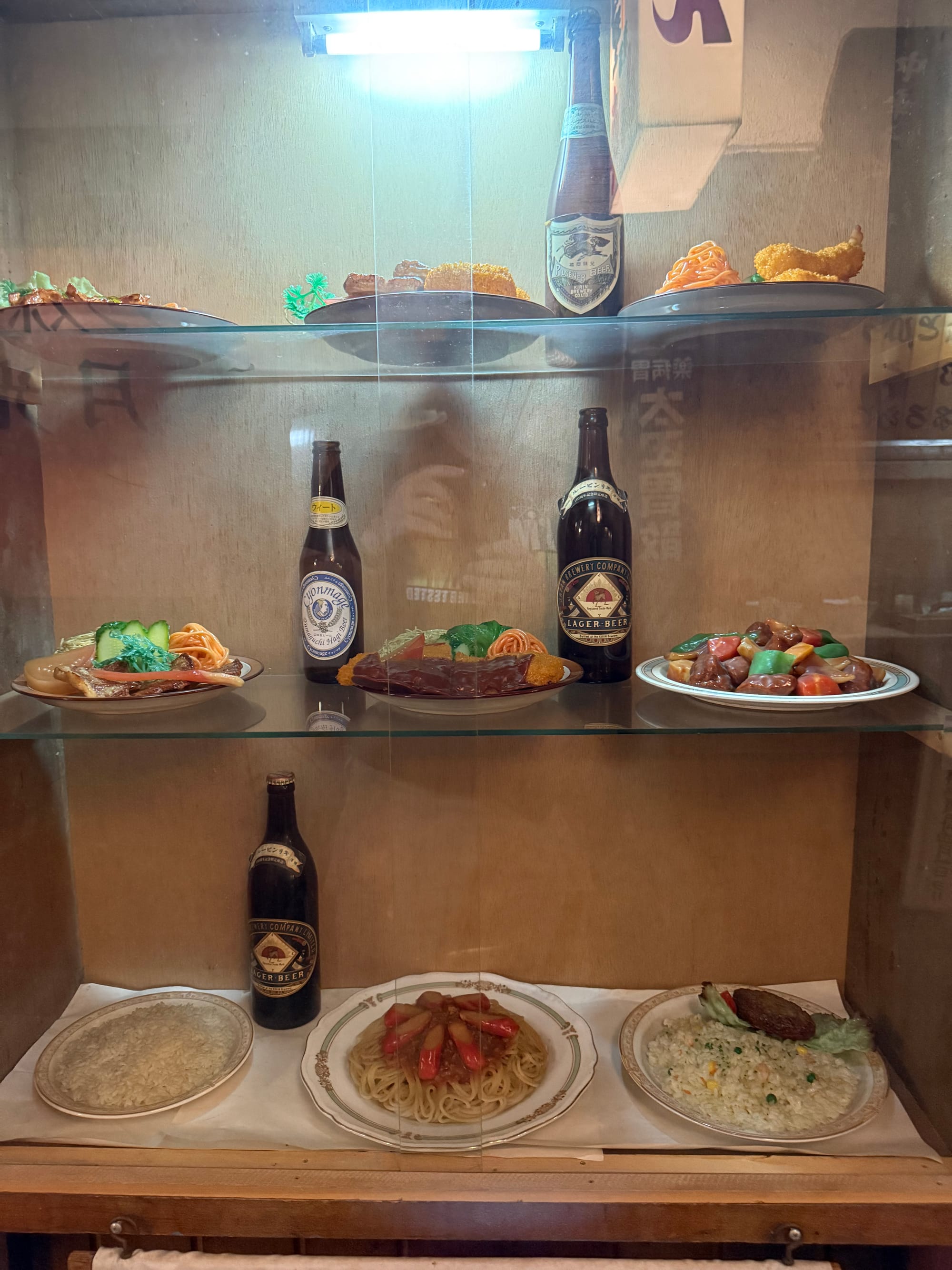 Display case of realistic plastic food models at the Takayama Showa-kan Museum, featuring replica meals, beer bottles and restaurant dishes typical of Japan's Showa era.