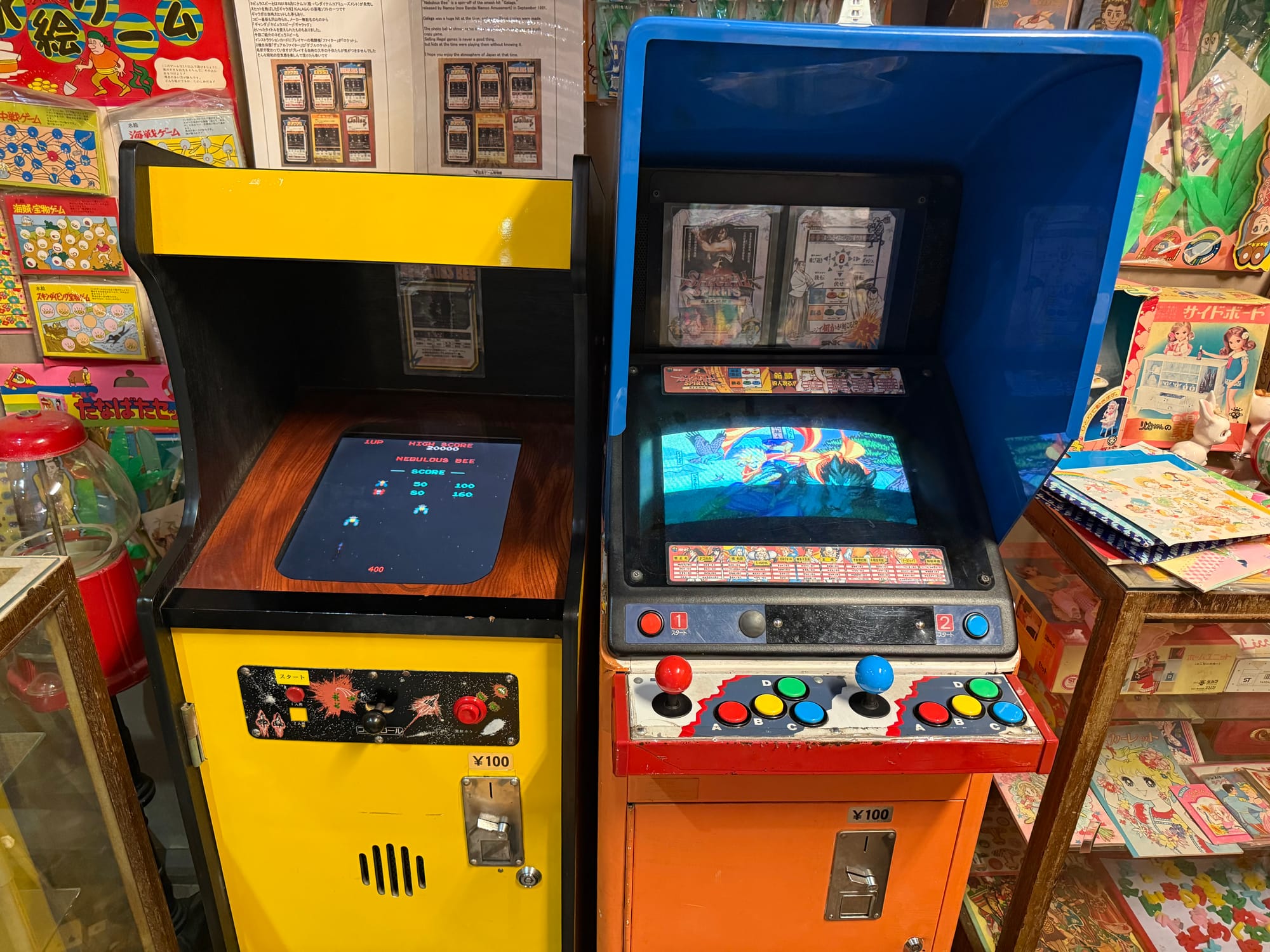 Vintage arcade machines at the Takayama Showa-kan Museum, including a tabletop shooting game and a standing video game cabinet with colourful controls and coin slots.