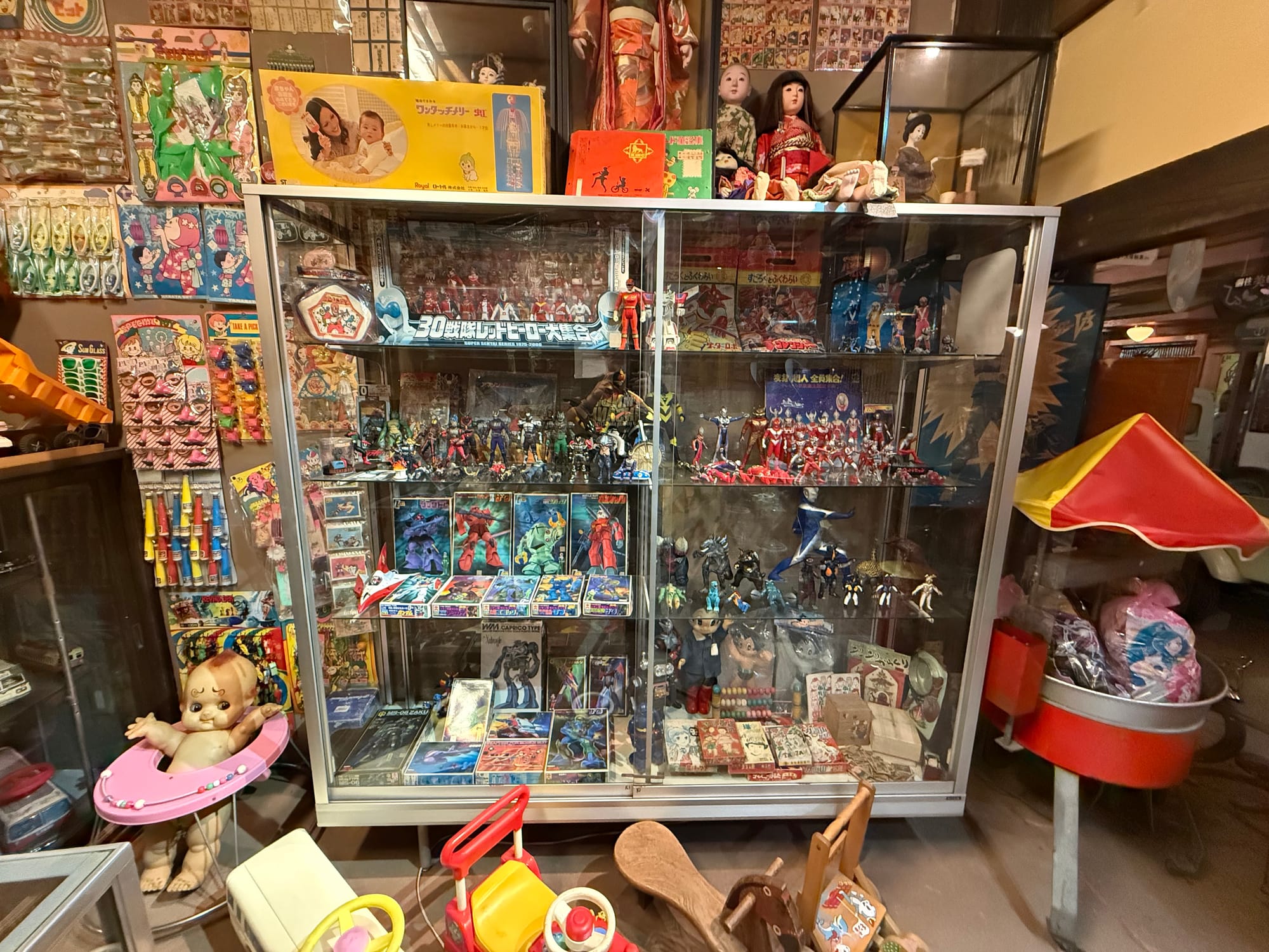 Display case at the Takayama Showa-kan Museum featuring vintage toys, anime figures, dolls, trading cards and superhero memorabilia from Japan's Showa era.