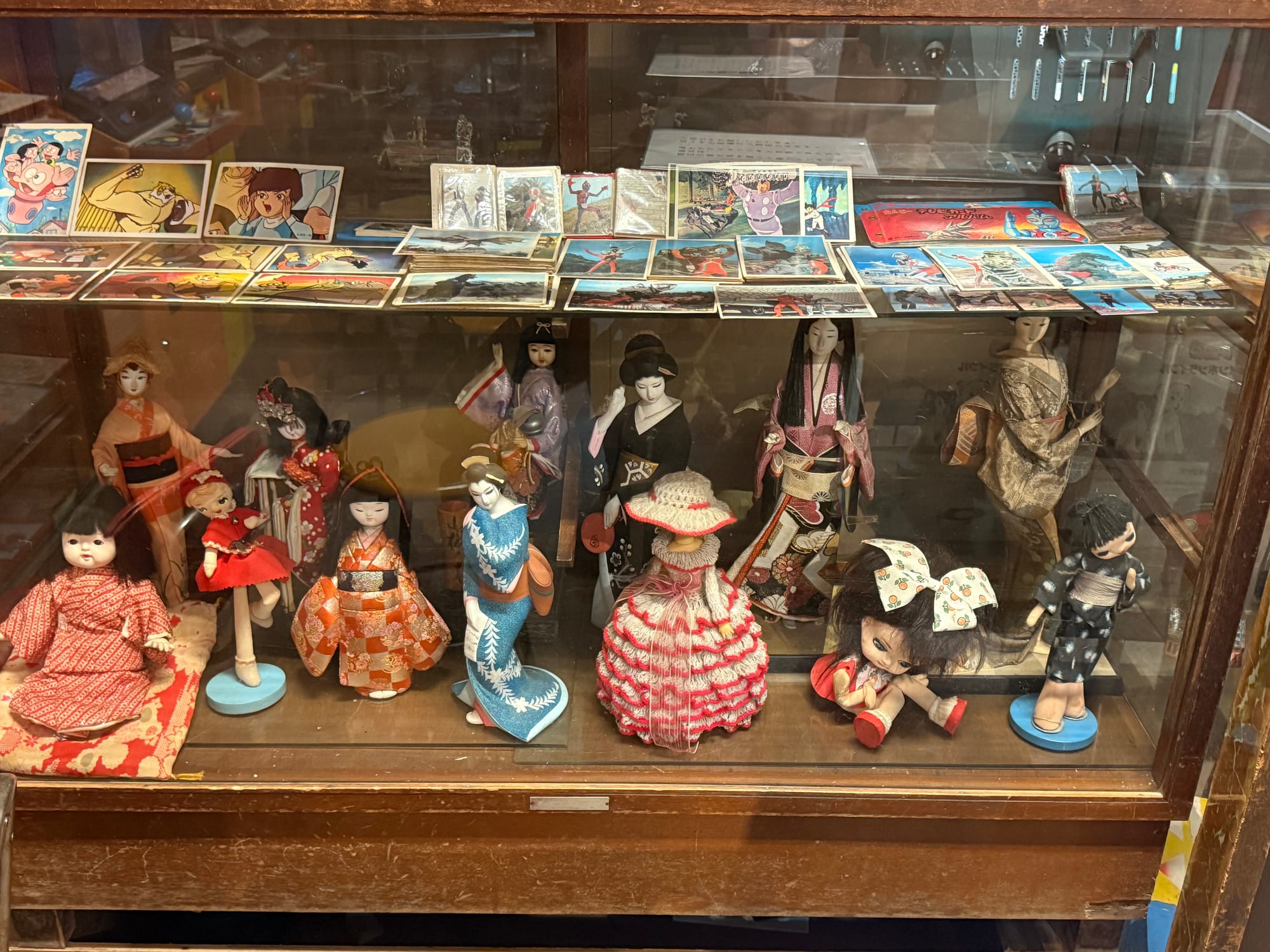 Display case at the Takayama Showa-kan Museum featuring traditional Japanese dolls, kimono-clad figures and collectible character cards from mid-20th-century Japan.