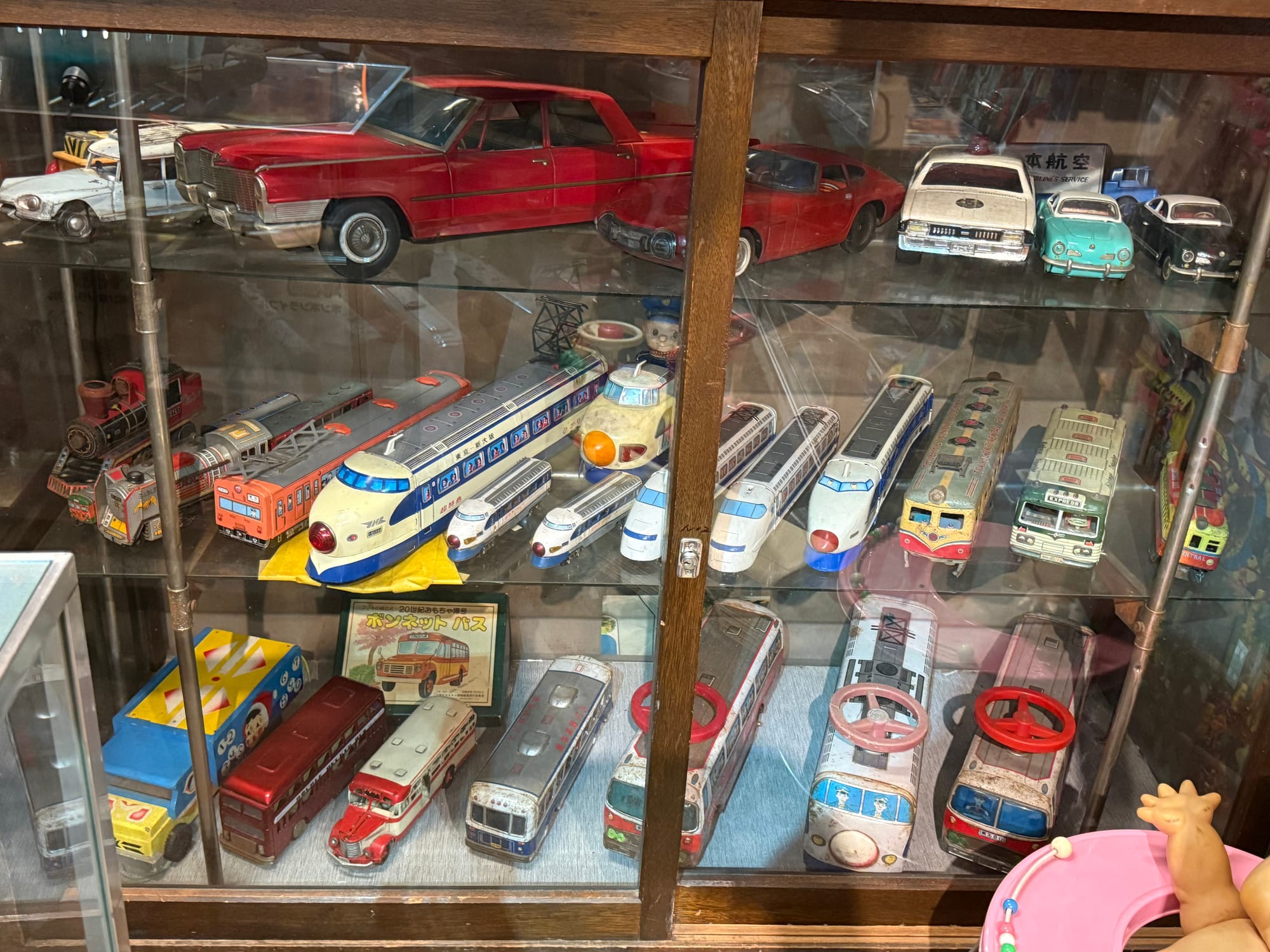 Display case at the Takayama Showa-kan Museum featuring vintage toy vehicles, including Shinkansen trains, buses, cars and locomotives from Japan's Showa era.