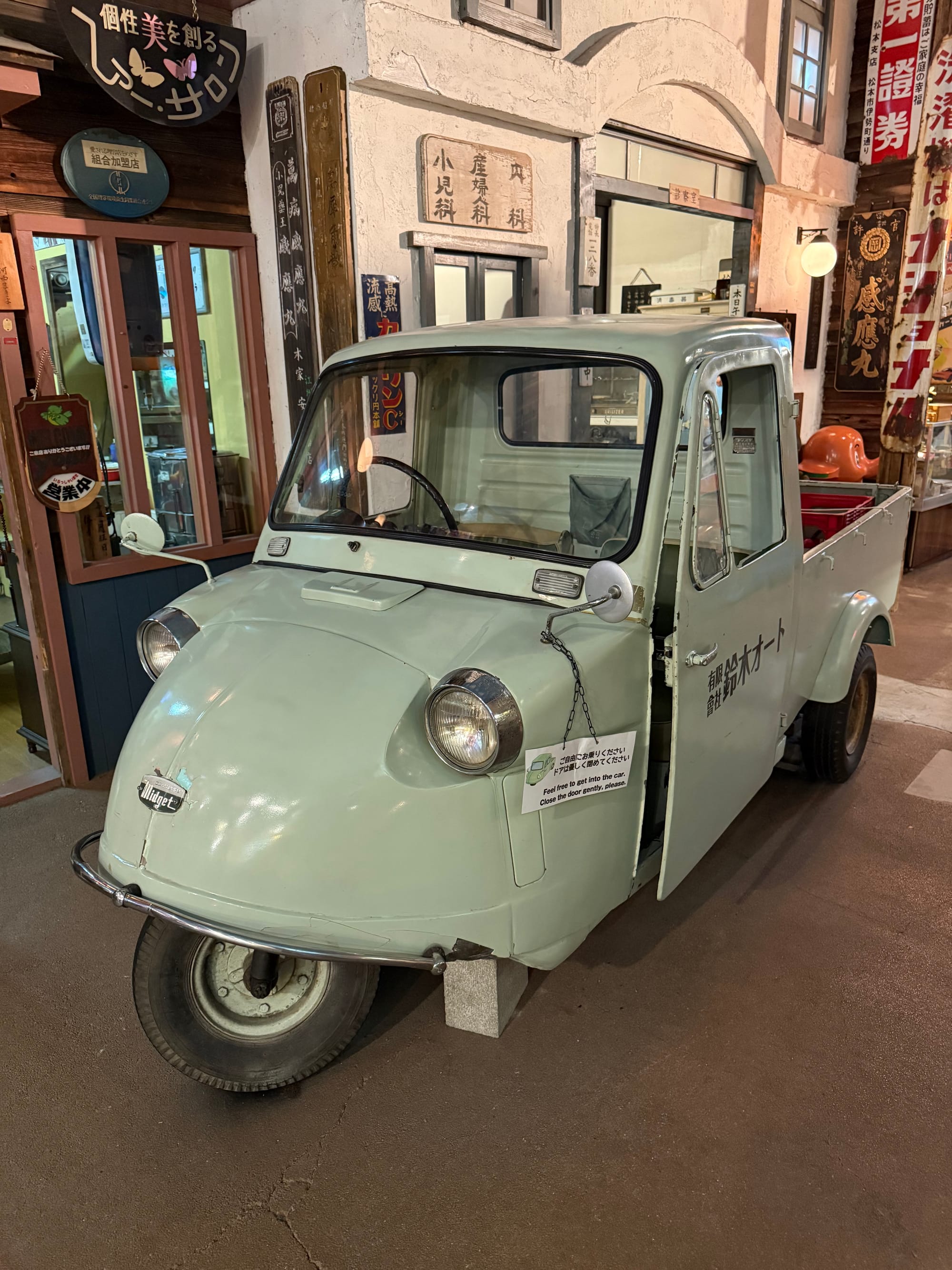Three-wheeled Midjet utility vehicle displayed at the Takayama Showa-kan Museum, featuring a compact cab, small cargo bed and distinctive rounded front-end design.