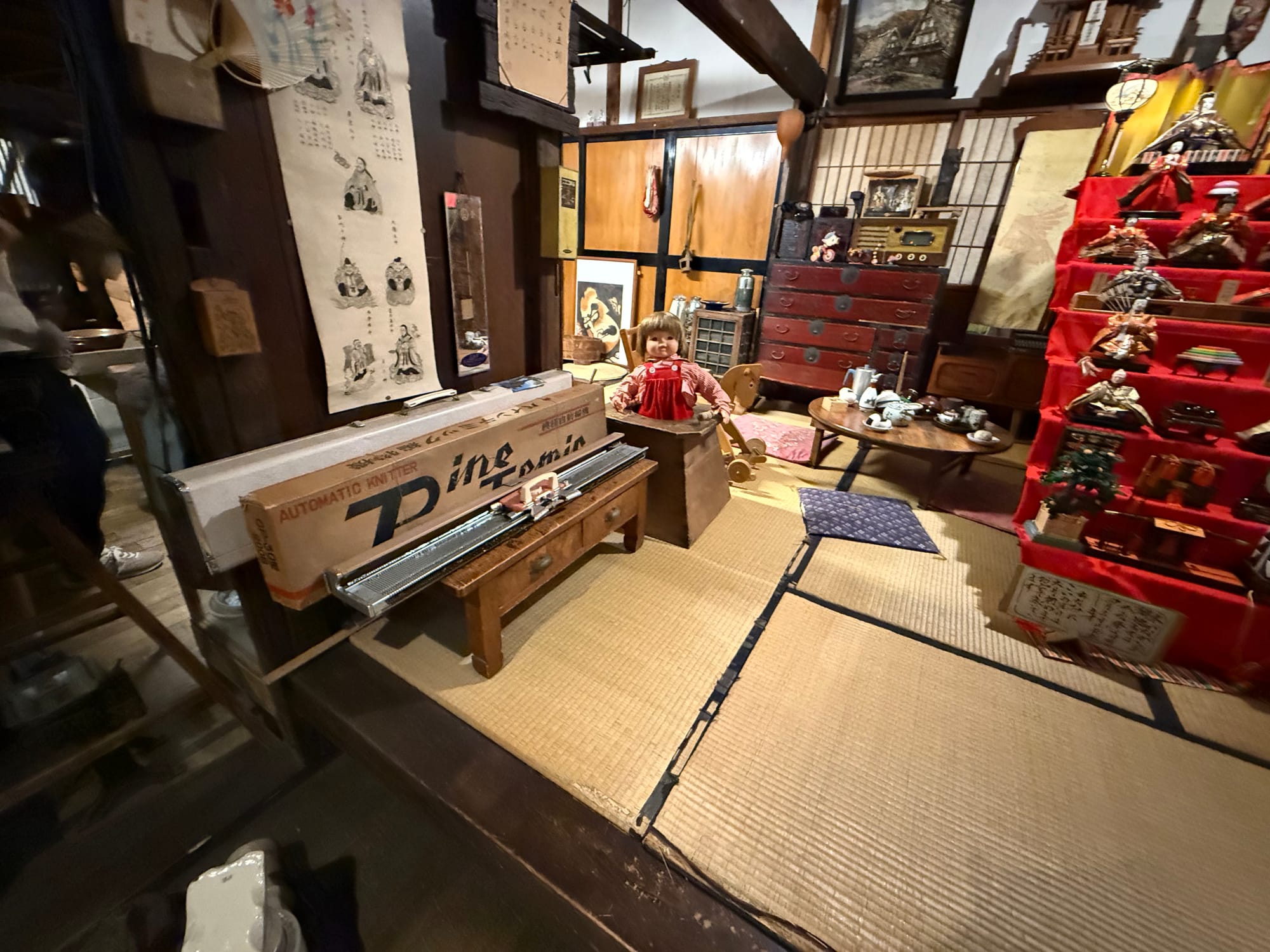Recreated Showa-era Japanese room at the Takayama Showa-kan Museum, featuring tatami mats, a knitting machine, traditional furniture, dolls and a Hinamatsuri display.