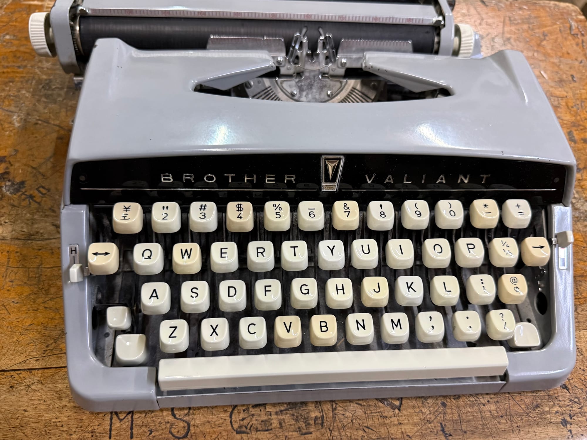 Brother Valiant typewriter displayed on a wooden school desk at the Takayama Showa-kan Museum, featuring English characters and a grey metal body.