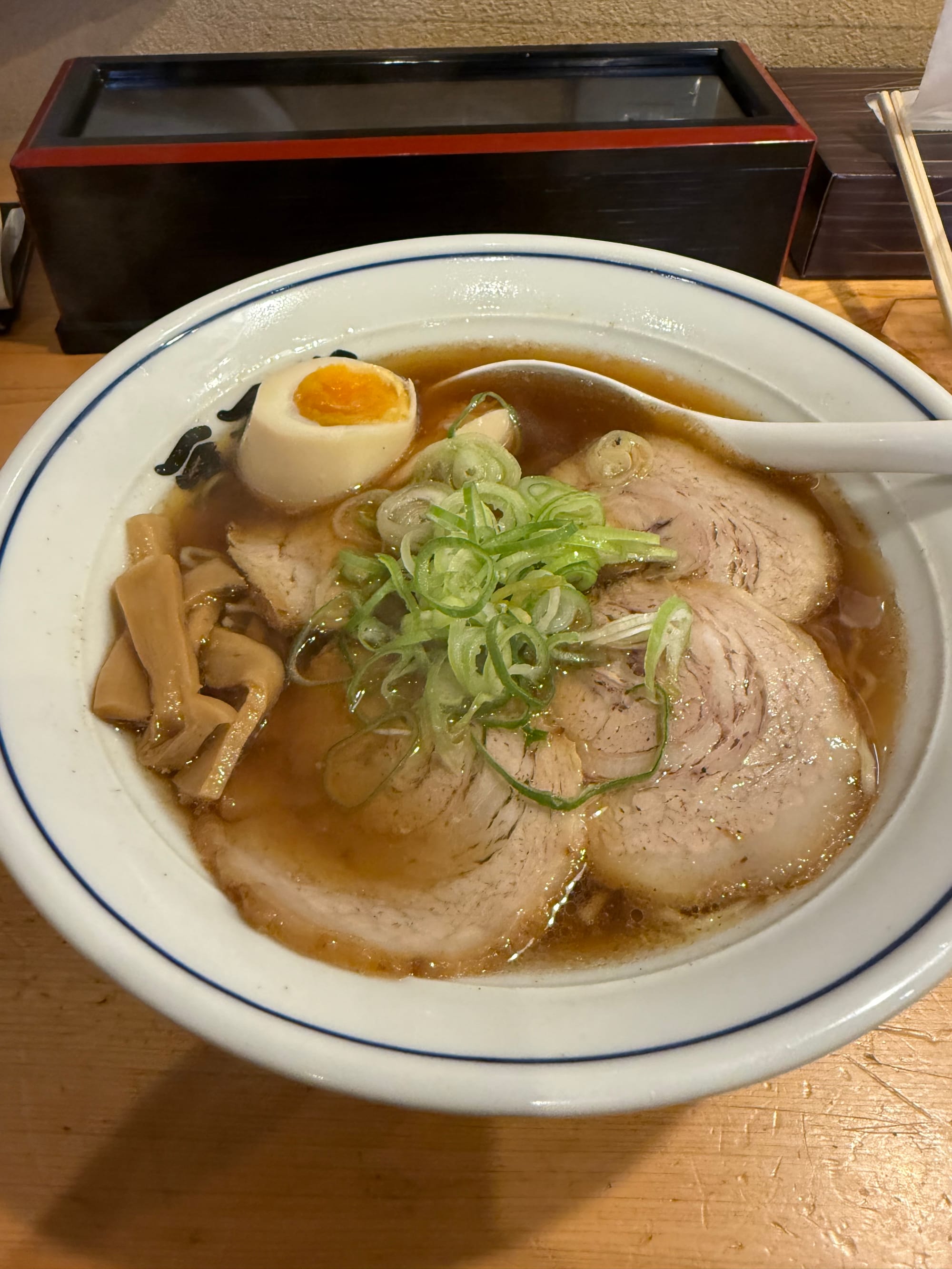 Bowl of shoyu ramen served in Takayama, topped with sliced chashu pork, half a soft-boiled egg, bamboo shoots and spring onions in a clear soy-based broth.