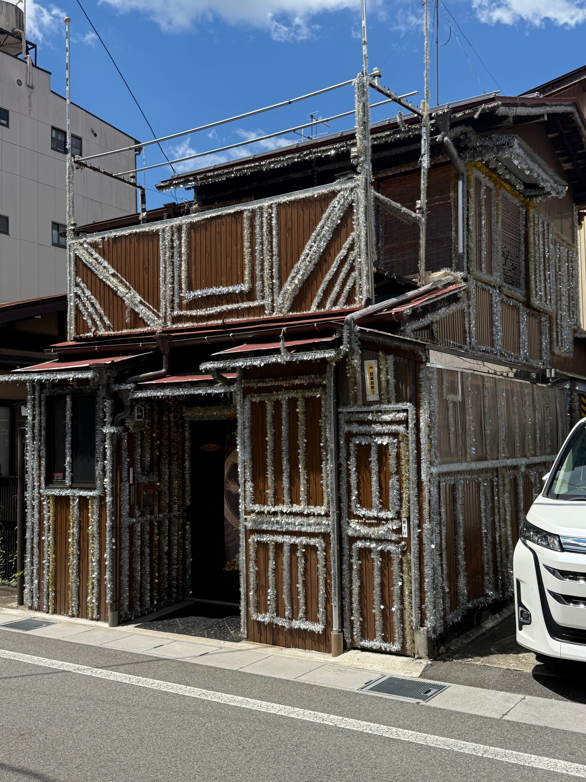 Traditional wooden building in Takayama decorated with silver tinsel from roof to ground level, creating a distinctive shimmering exterior beneath a bright blue summer sky.