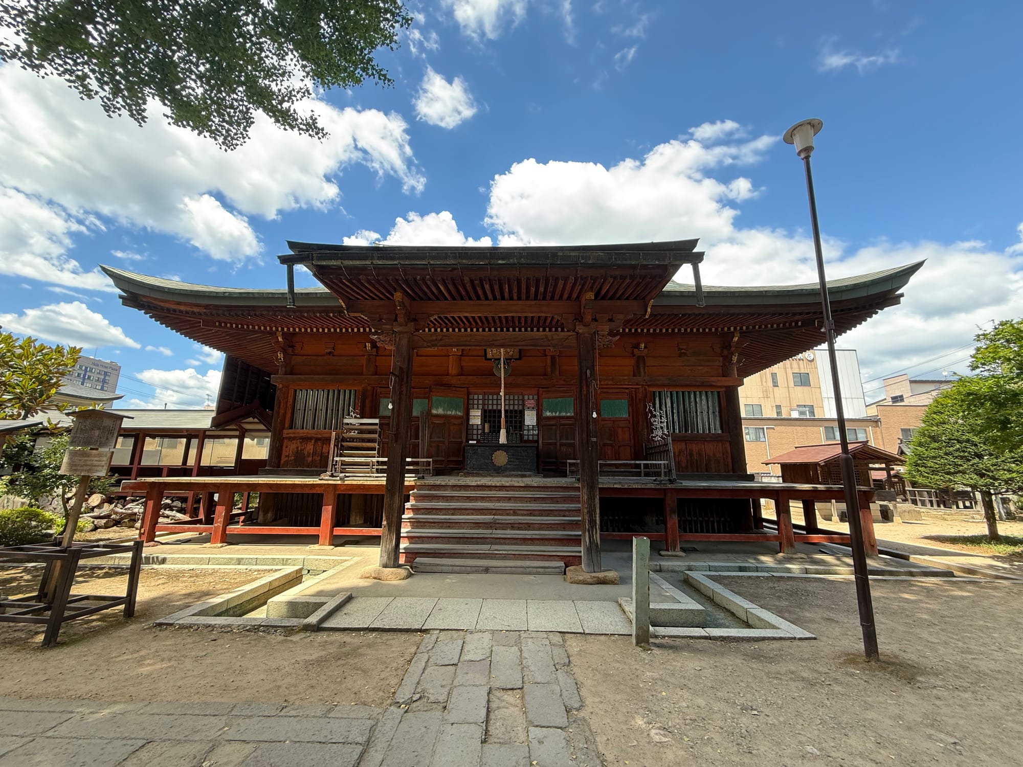 Main hall of Hida Kokubun-ji Temple in Takayama, featuring traditional wooden architecture, broad sweeping eaves, stone steps and a courtyard beneath a bright summer sky.