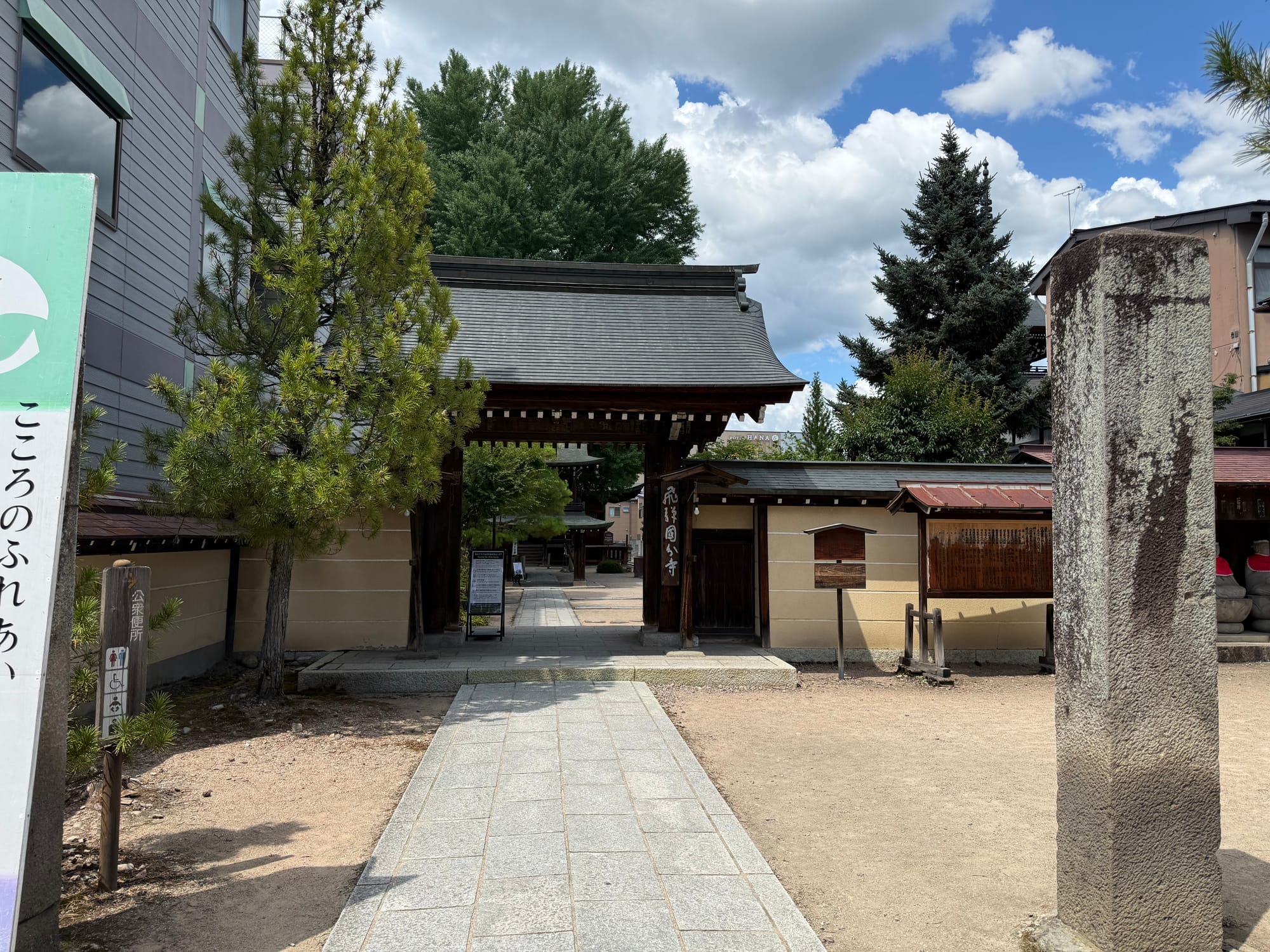 Main gate of Hida Kokubun-ji Temple in Takayama, featuring traditional wooden architecture, a stone pathway and a temple nameboard beneath dramatic summer clouds.