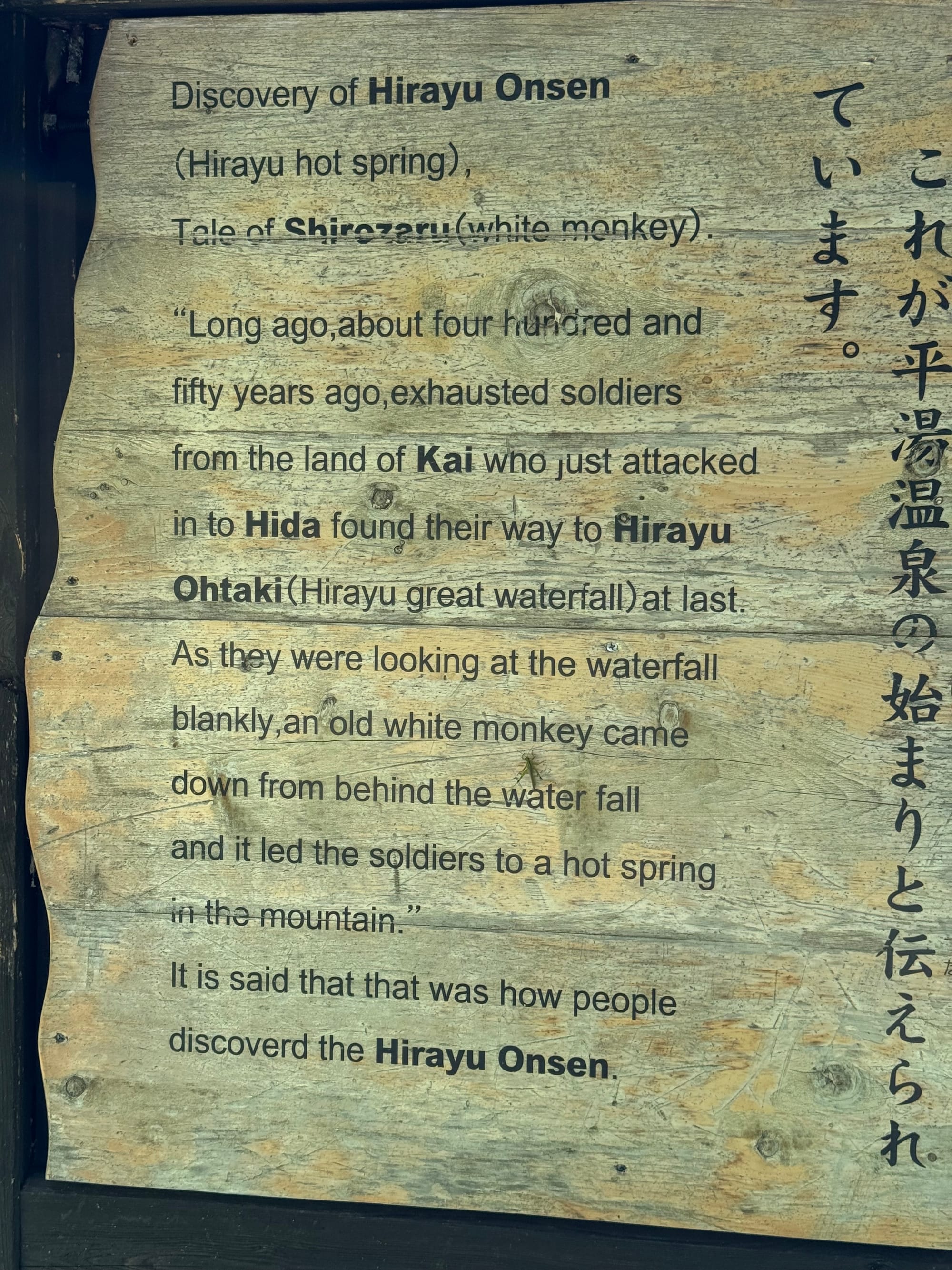 Interpretive sign at Hirayu Great Falls describing the legend of the discovery of Hirayu Onsen, featuring English and Japanese text on a weathered wooden information board.