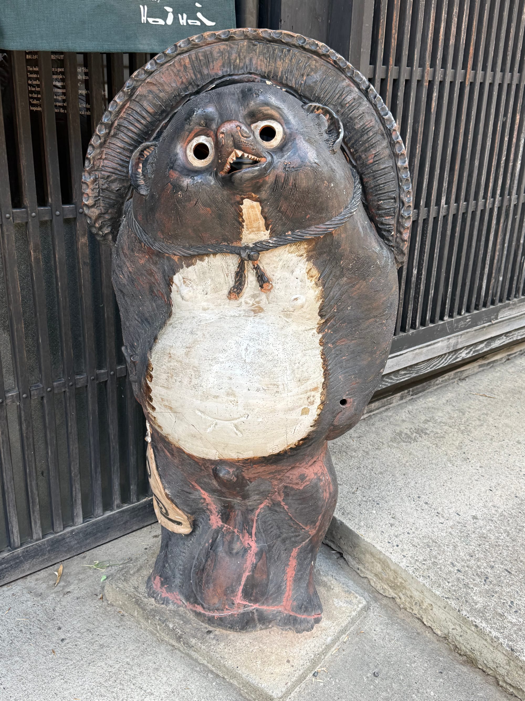 Ceramic tanuki statue outside a building in Narai-juku, depicting the folkloric Japanese raccoon dog wearing a straw hat and standing beside a traditional wooden façade.