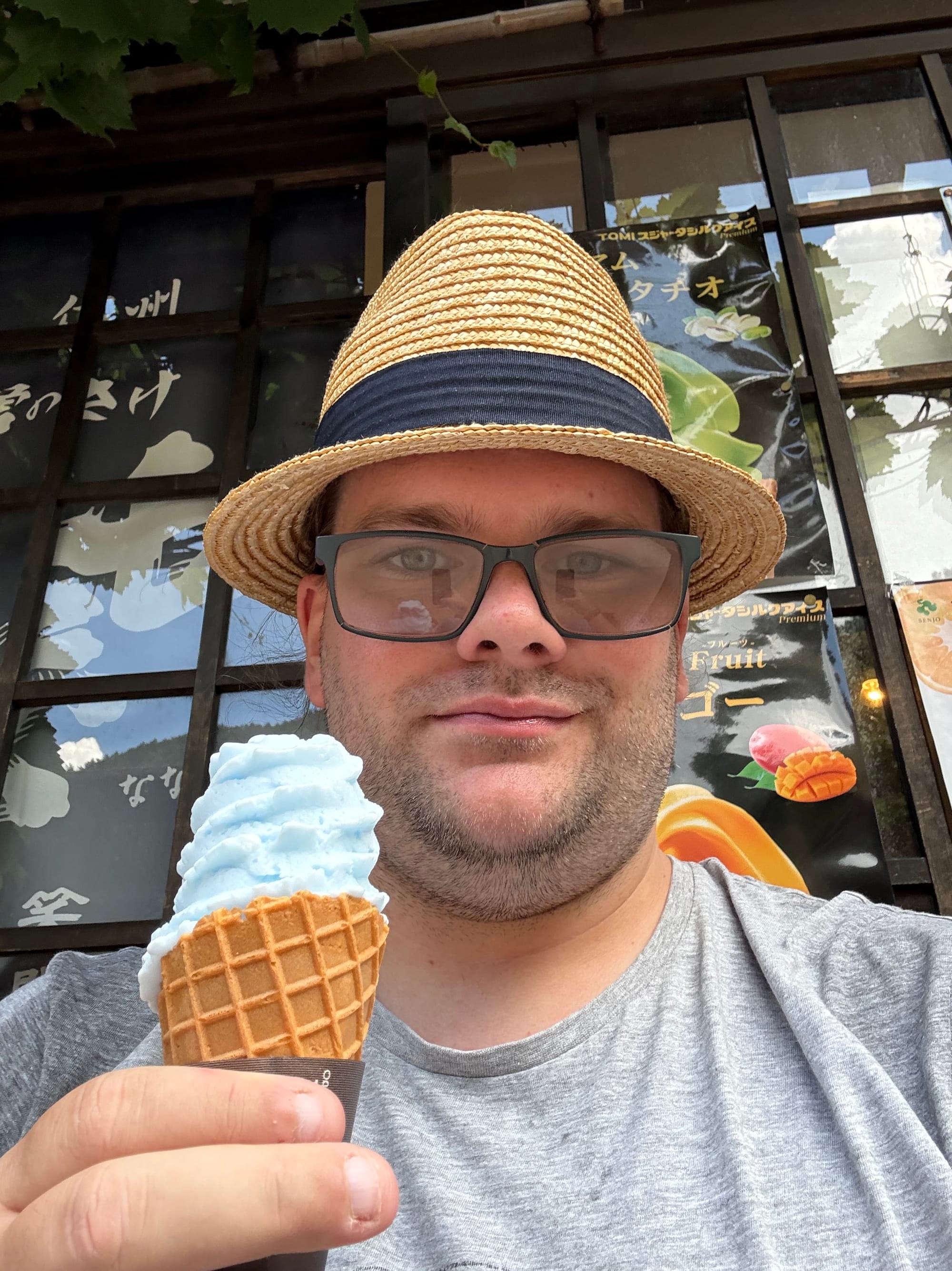Person holding a blue ramune-flavoured soft-serve ice cream cone in Narai-juku, with traditional wooden buildings and ice cream advertisements visible in the background.