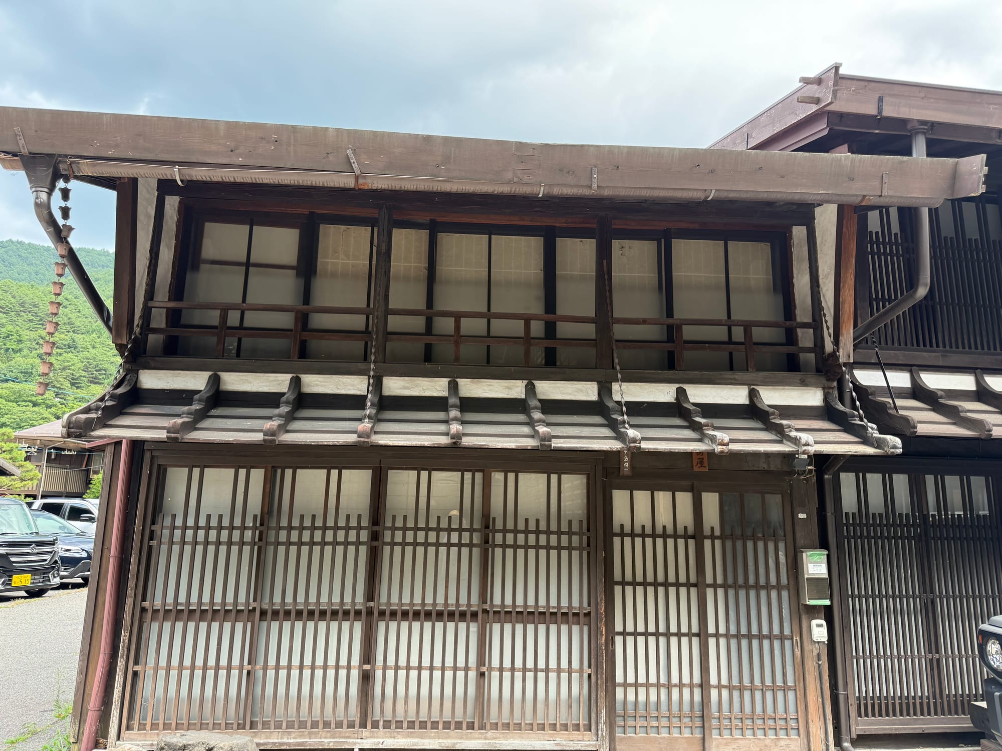 Traditional wooden townhouse in Narai-juku, featuring lattice windows, sliding doors, white plaster walls and a sheltered upper-floor balcony typical of Edo-period architecture.